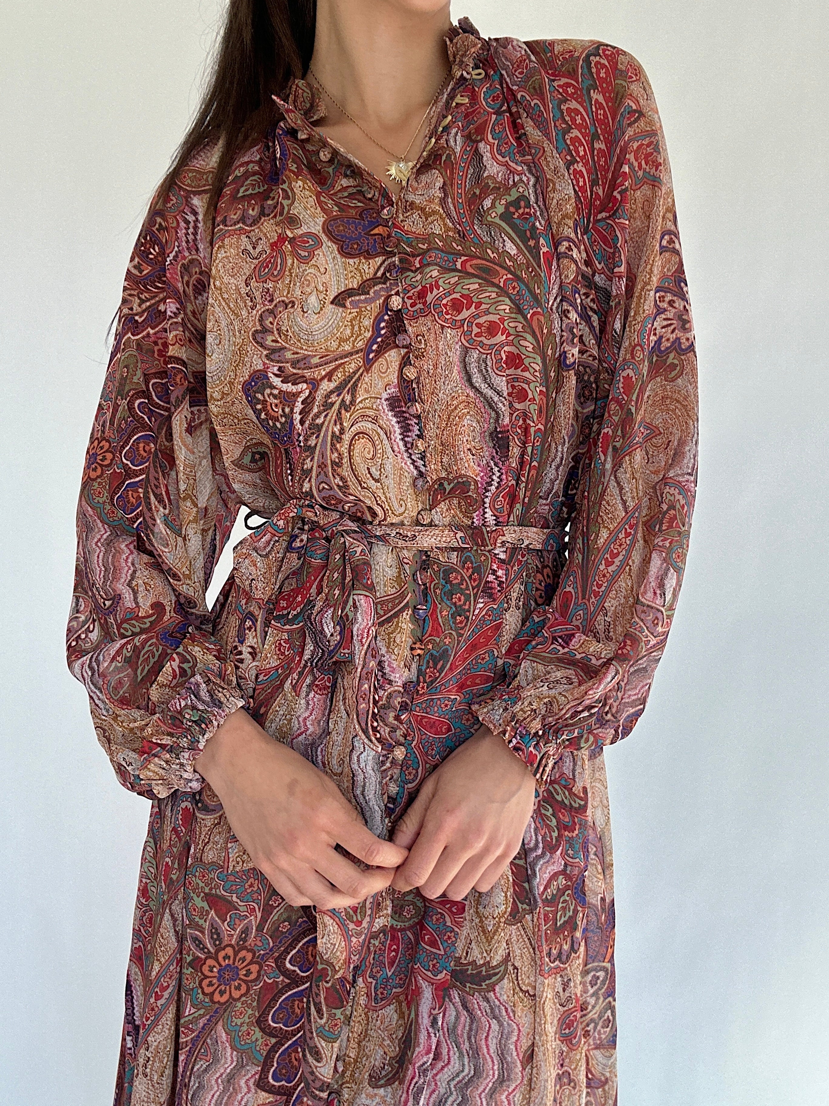 Person wearing a long-sleeve, boho paisley patterned dress against a plain background showing off the neckline, button front and waist tie
