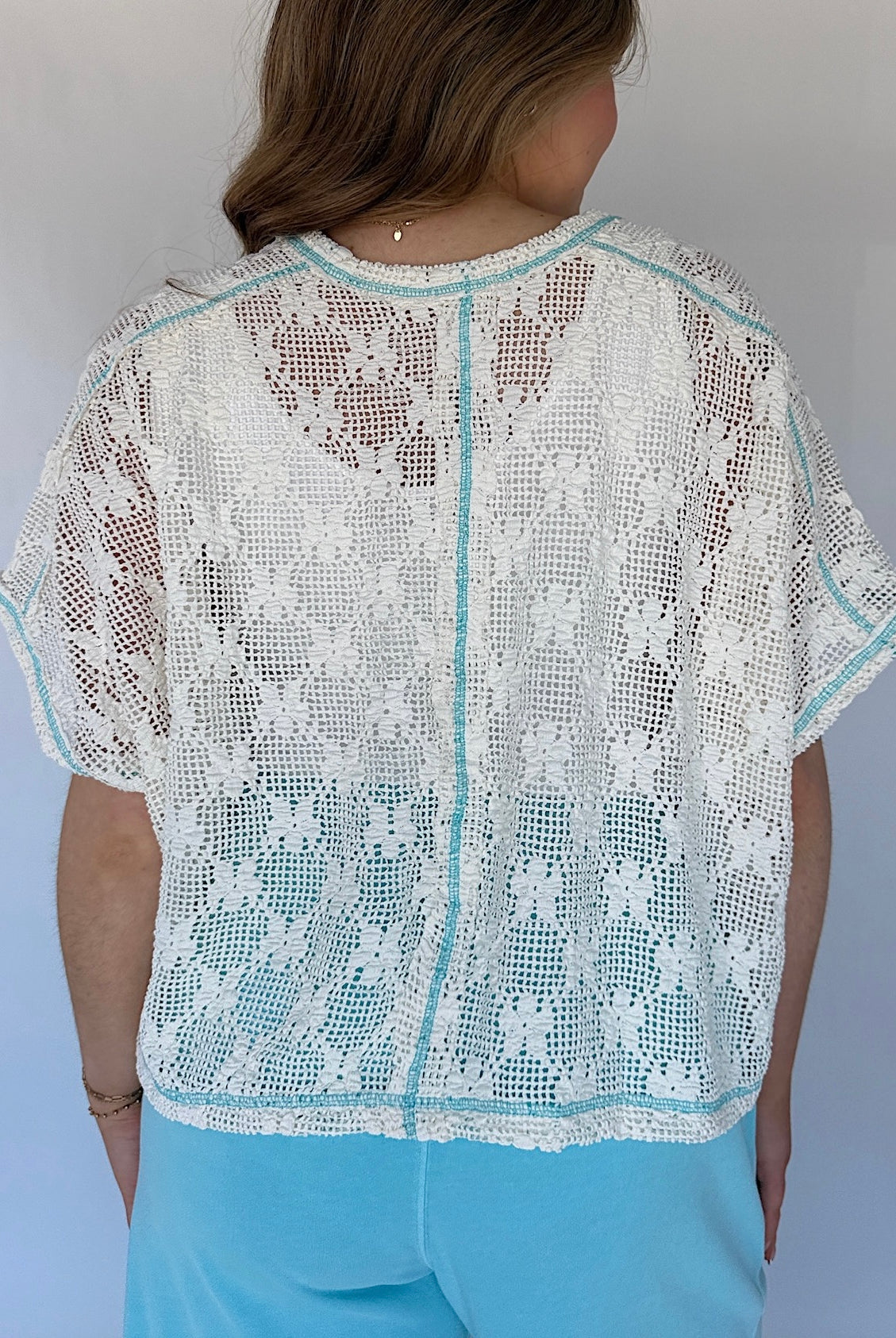 Person wearing a white lace top with short sleeves against a plain background