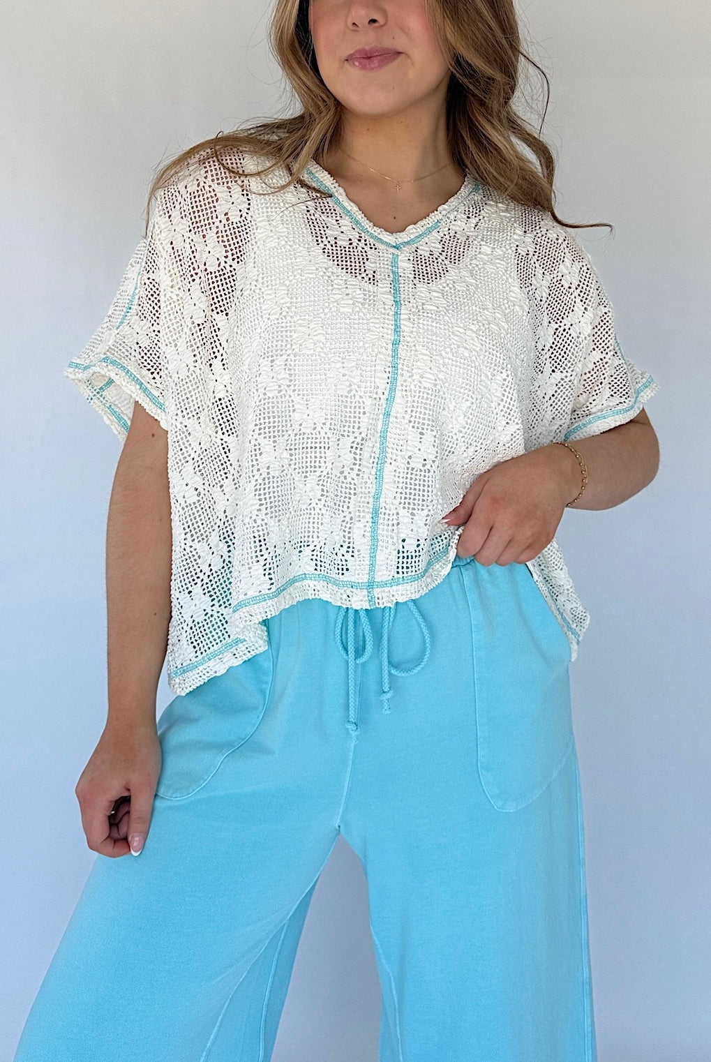 Woman wearing a white lace top and light blue pants against a plain background