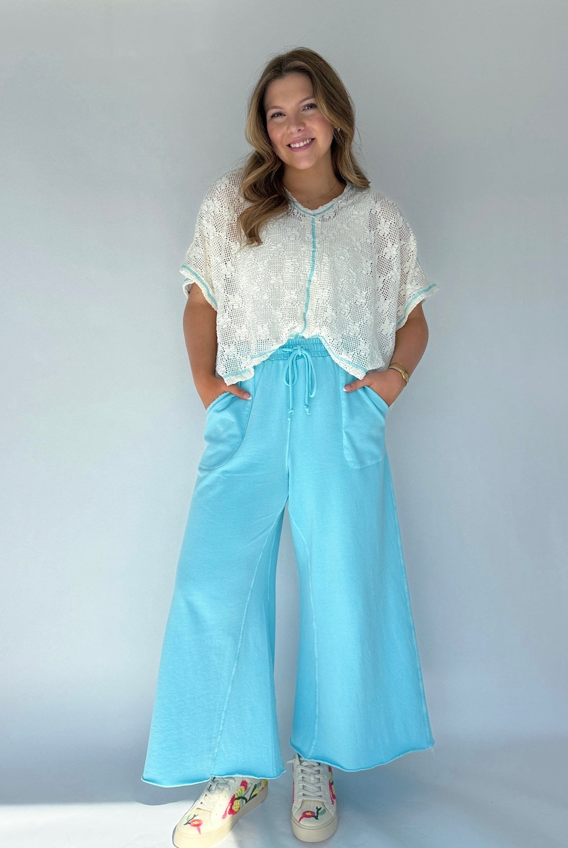 Person wearing a white lace top and light blue wide-leg pants on a plain background
