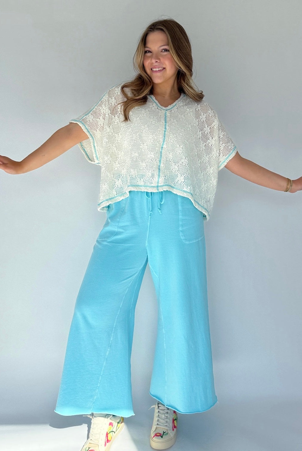 Woman wearing a light-colored top and light blue pants against a plain background