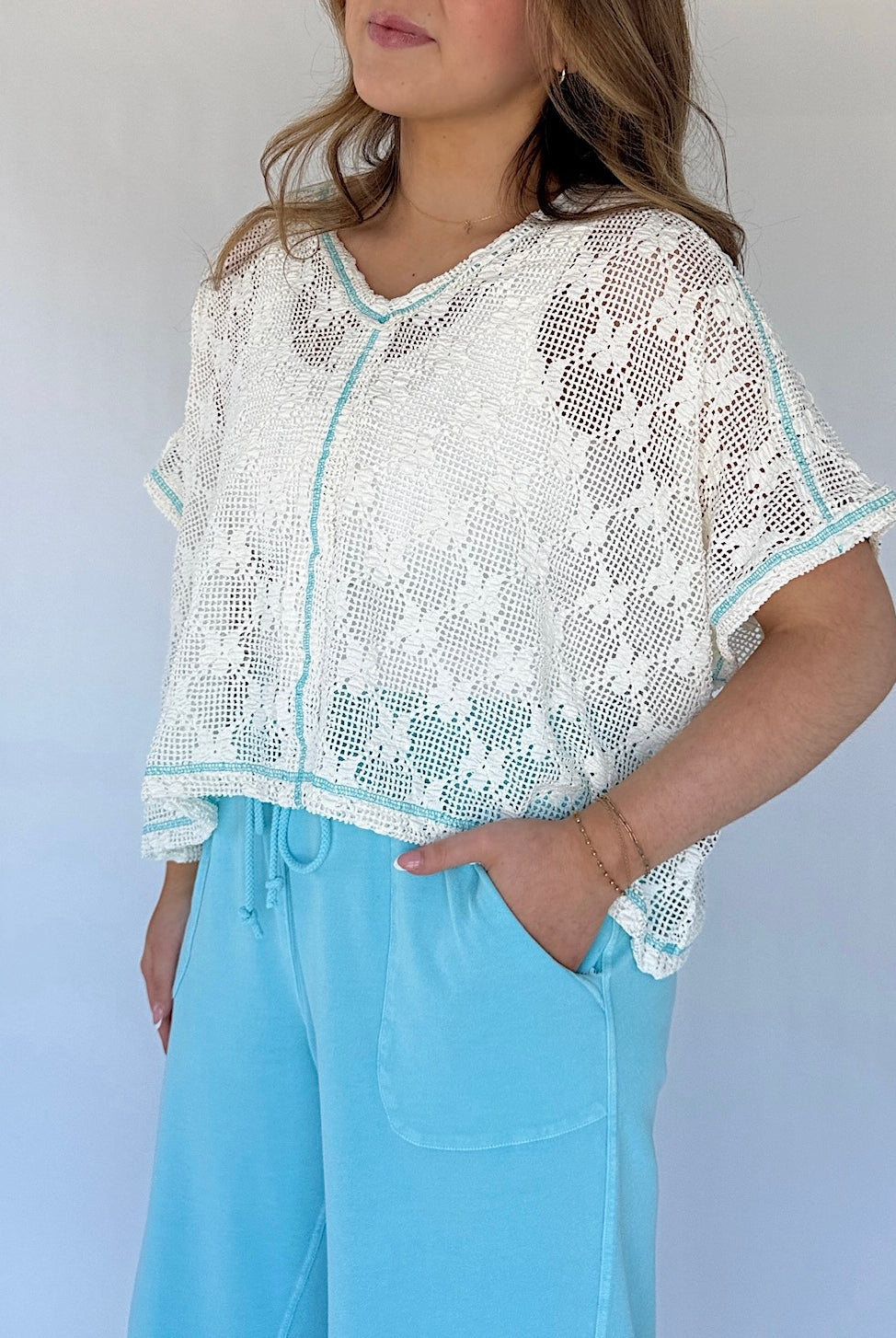 Person wearing a white lace top with blue trim and light blue pants against a plain background