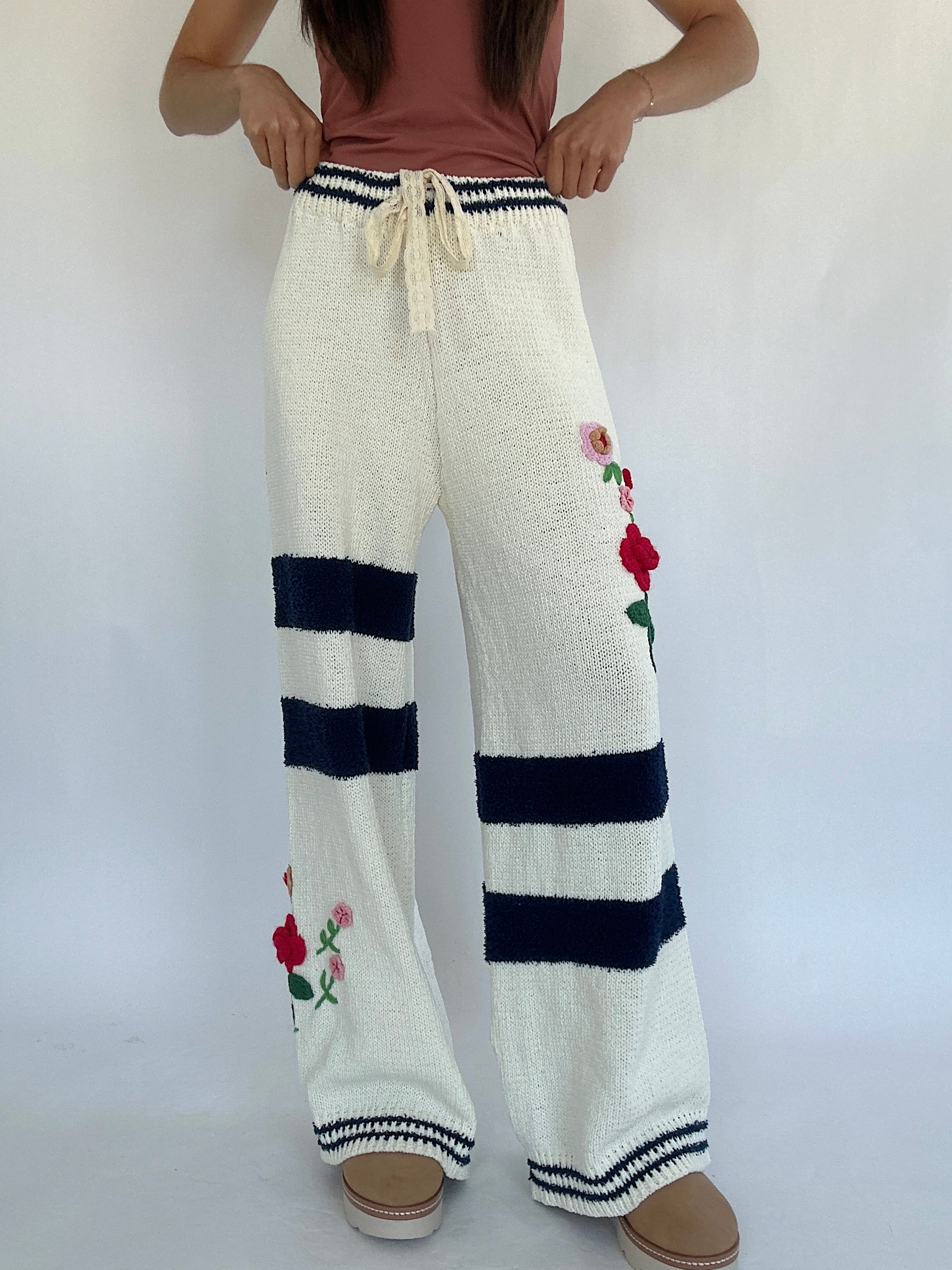 White knitted pants with navy stripes and floral embroidery on a white background