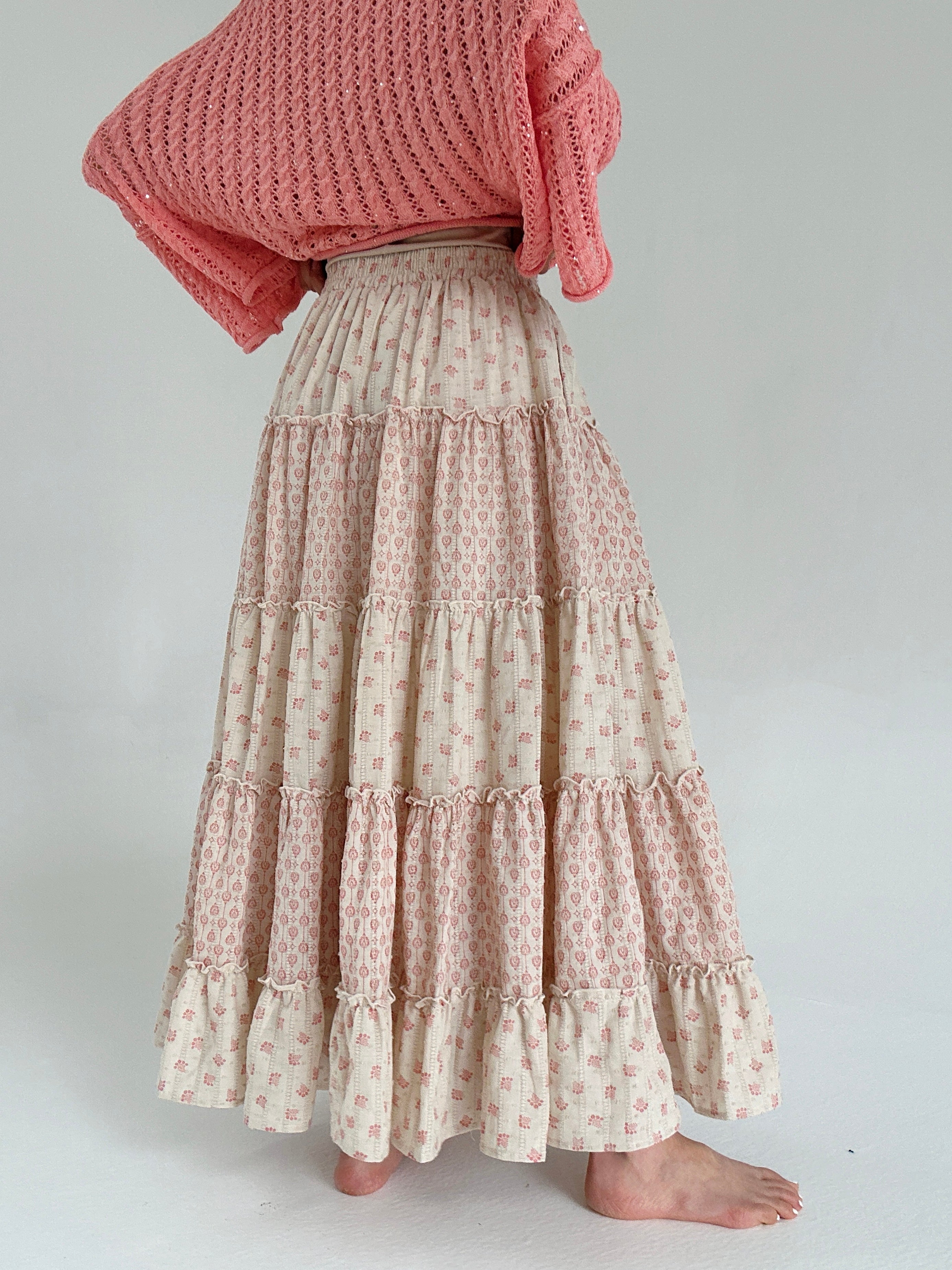 Person wearing a beige and coral patterned skirt and coral top on a white background