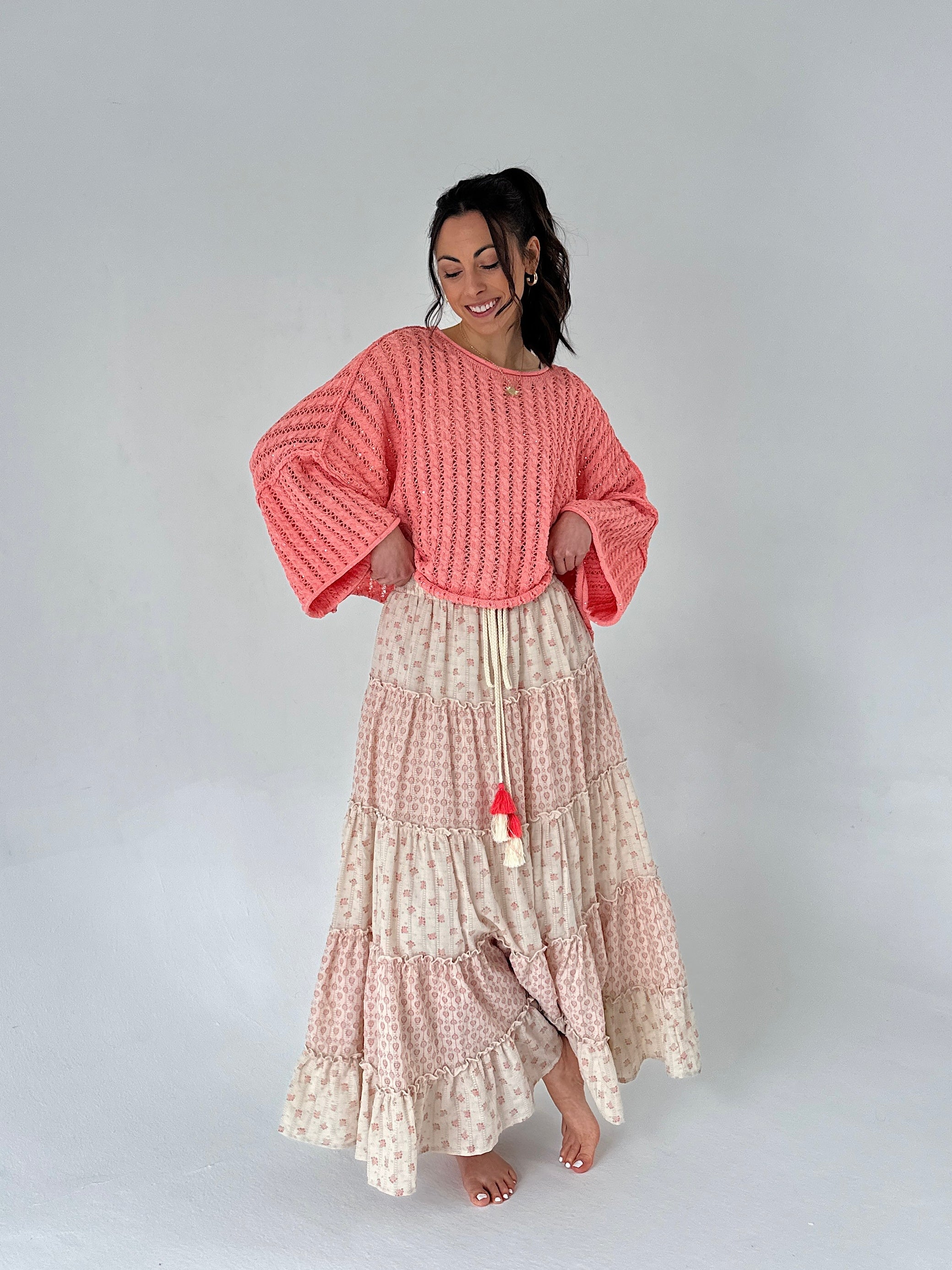 Woman wearing a coral sweater and patterned skirt on a plain background
