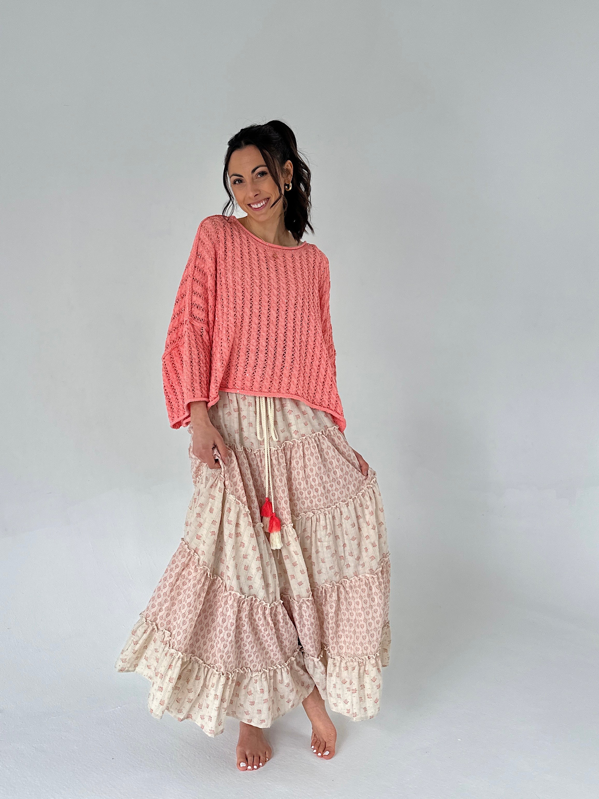Woman wearing a coral sweater and patterned skirt on a plain background