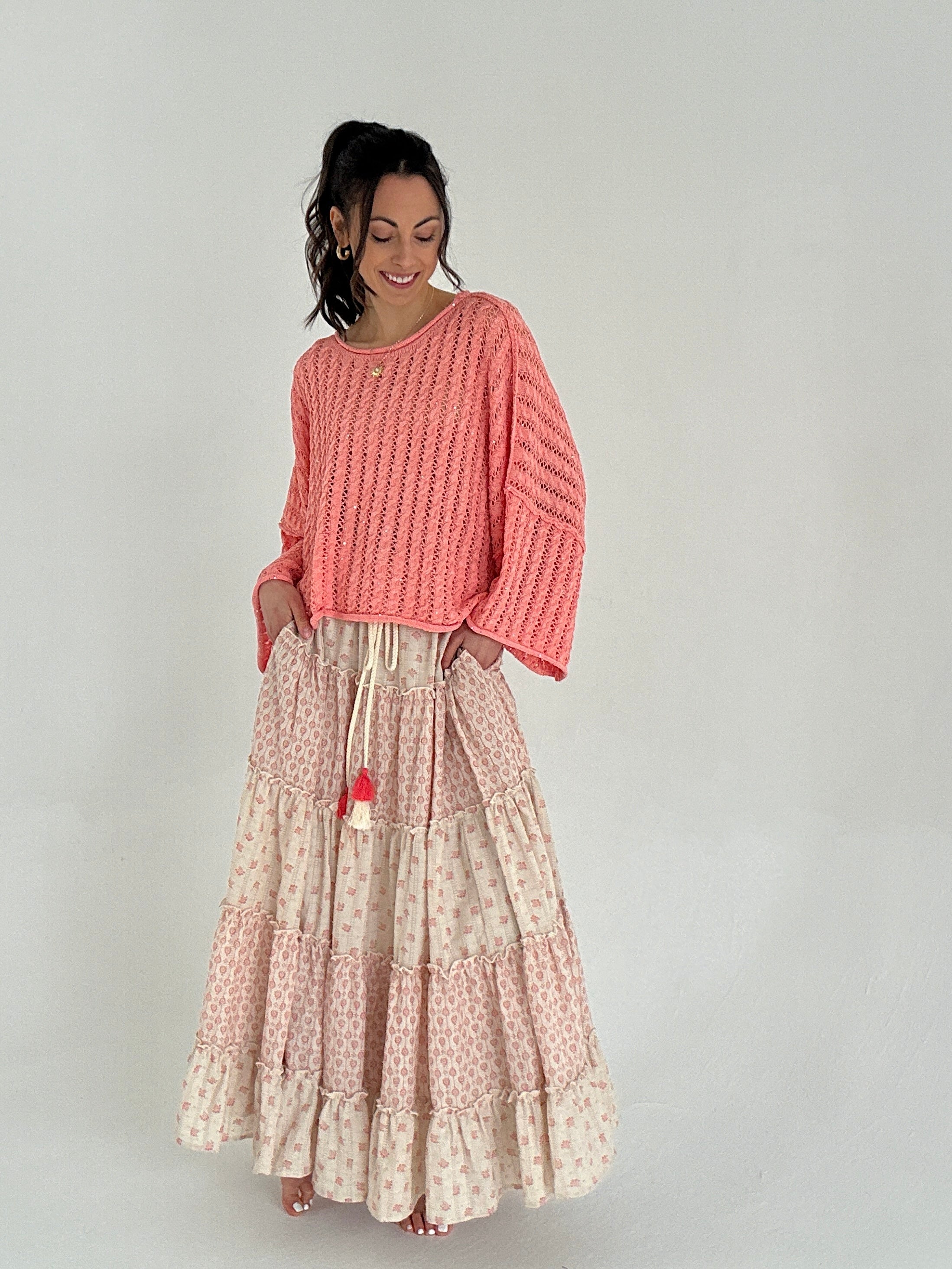 Woman wearing a coral sweater and patterned skirt on a plain background showing side pockets