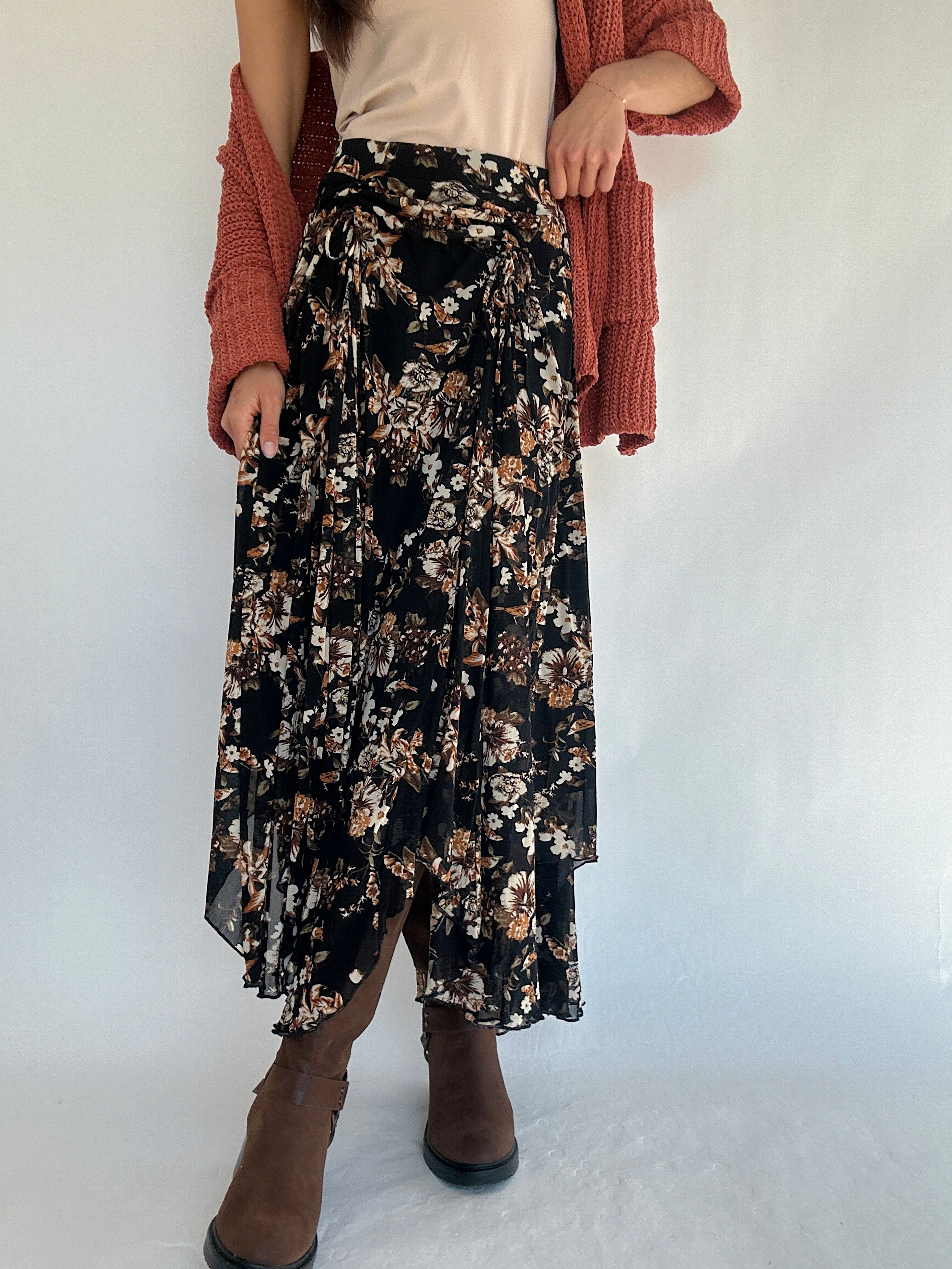 Person wearing a black floral skirt and rust cardigan on a white background