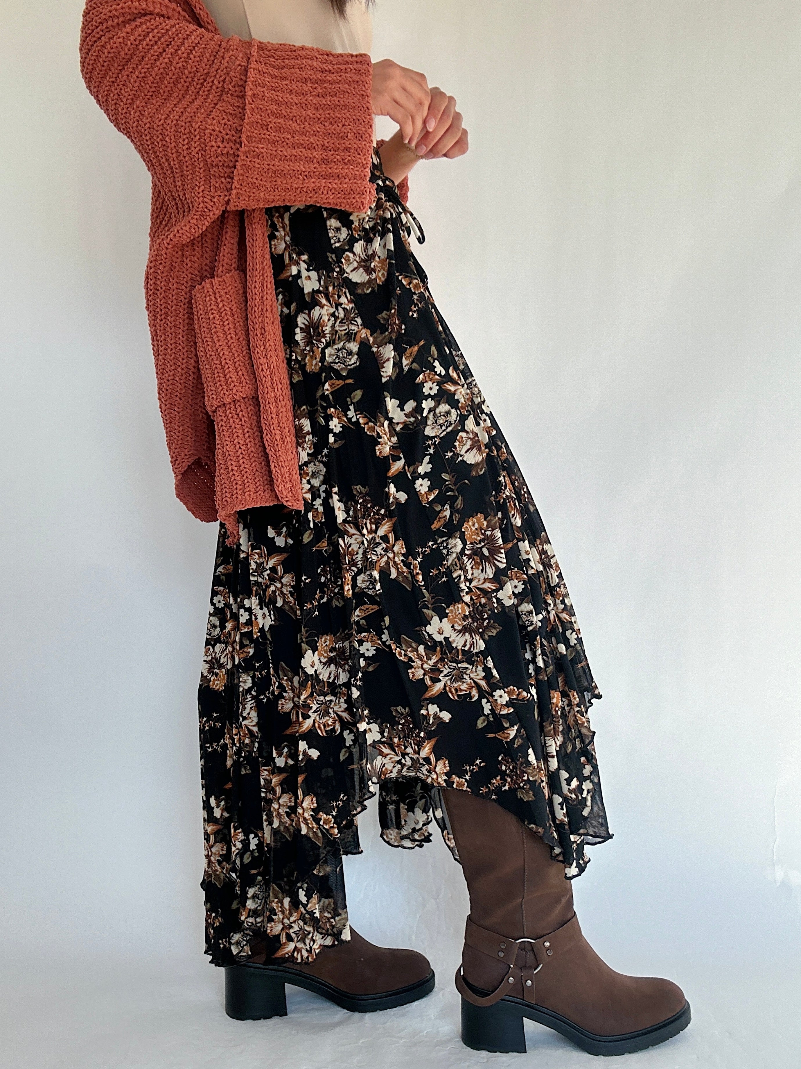 Person wearing a floral dress, rust cardigan, and boots on a white background from side