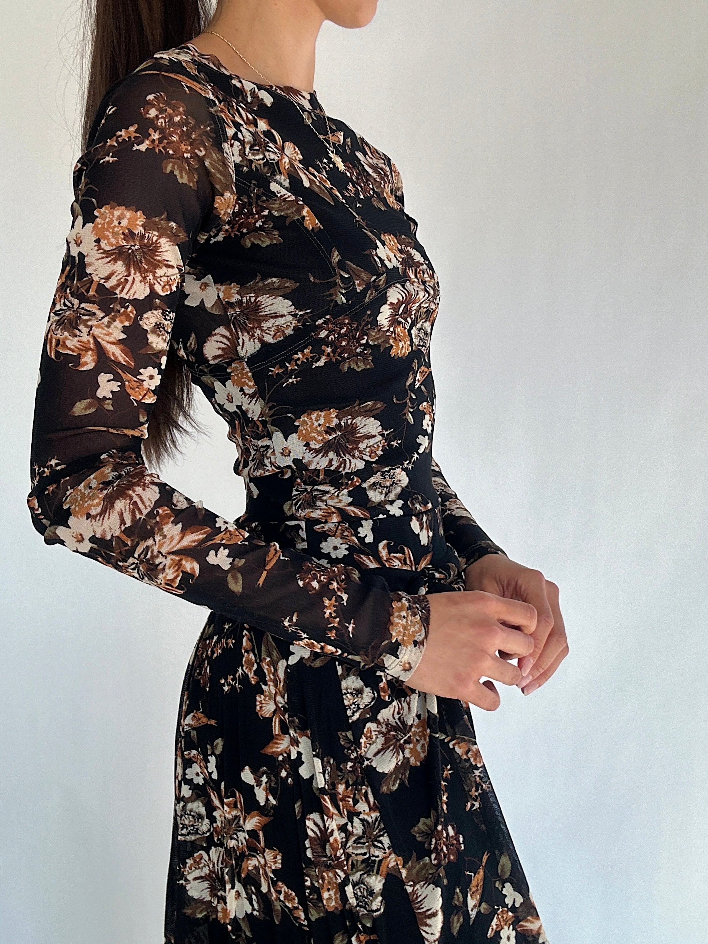 Black floral long sleeve top worn by a person on a white background showing side