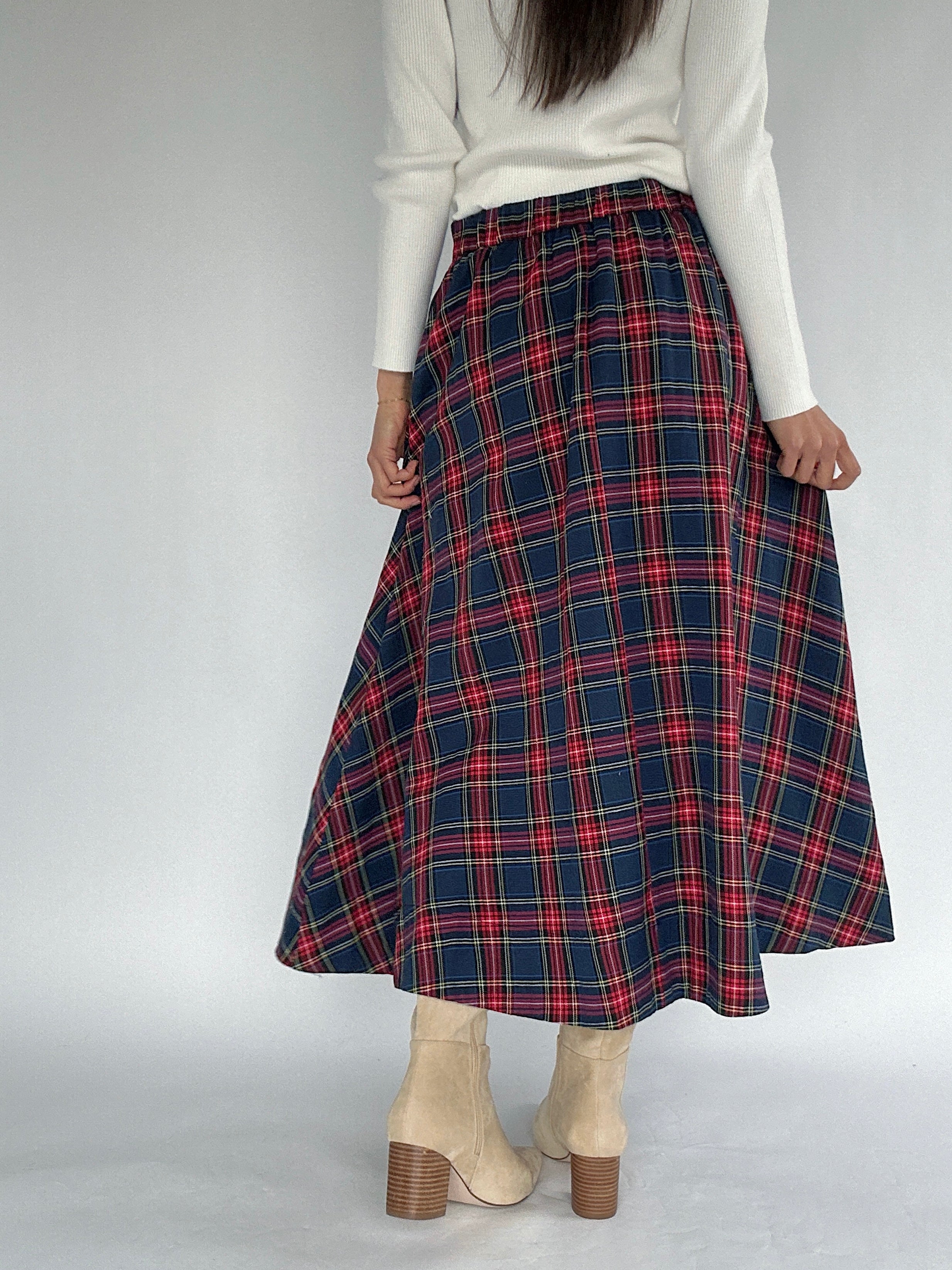 Person wearing a red and blue plaid skirt on a plain background back side