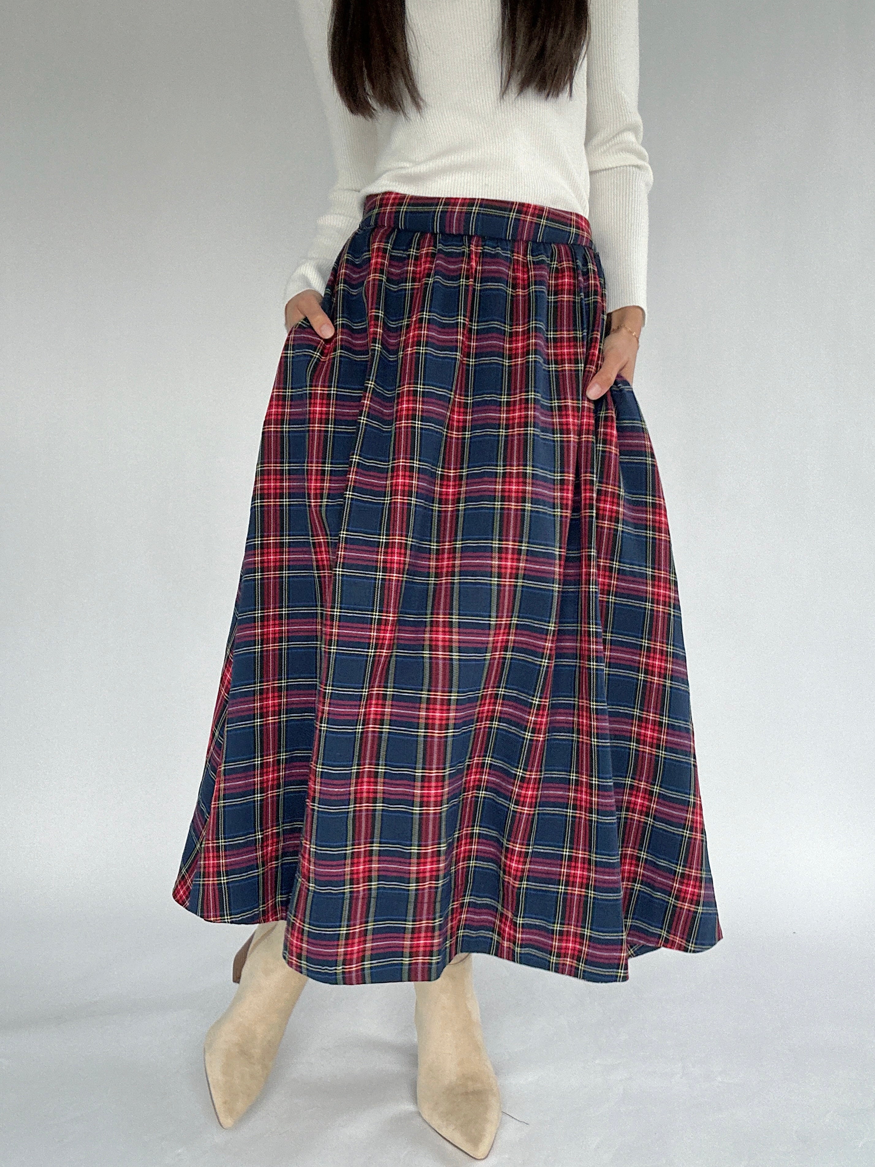 Person wearing a red and navy blue plaid midi skirt on a plain background