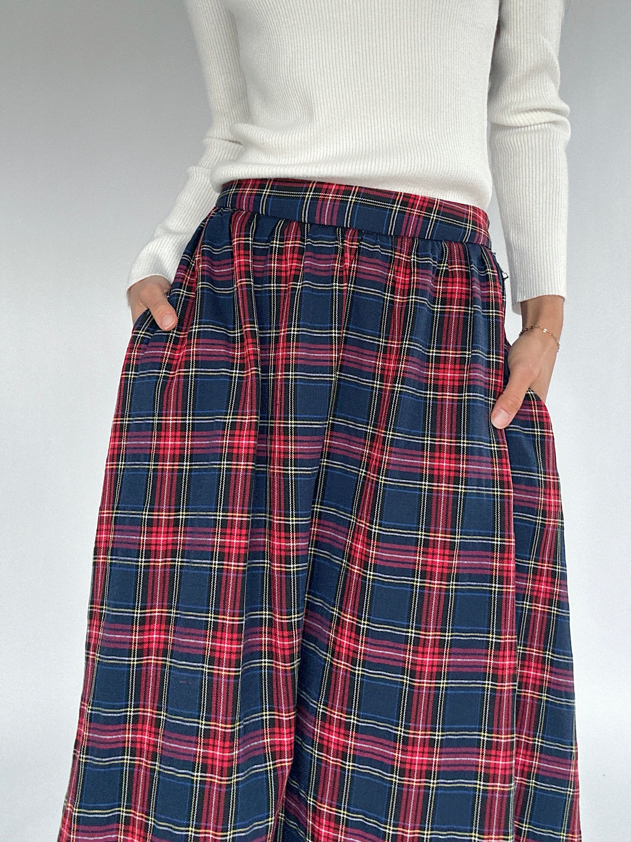 Plaid skirt worn with a white sweater on a plain background showing elastic waist and side pockets