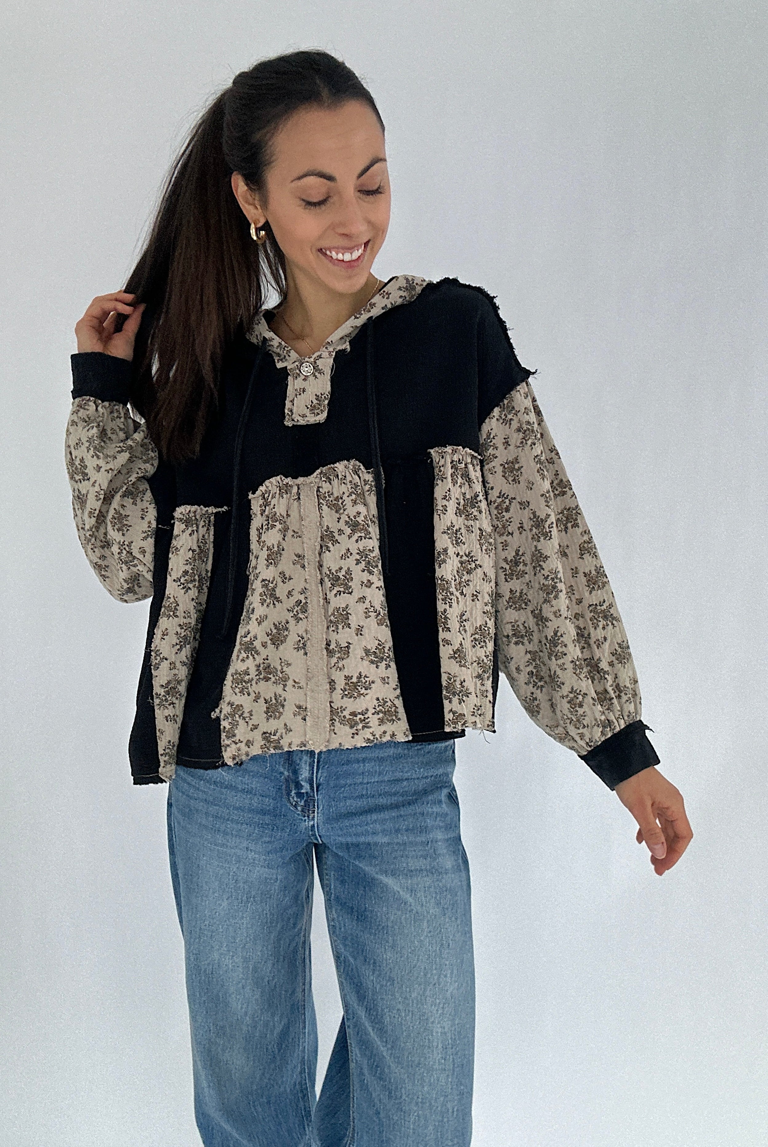 Woman wearing a black and floral-patterned hoodie top with blue jeans on a white background