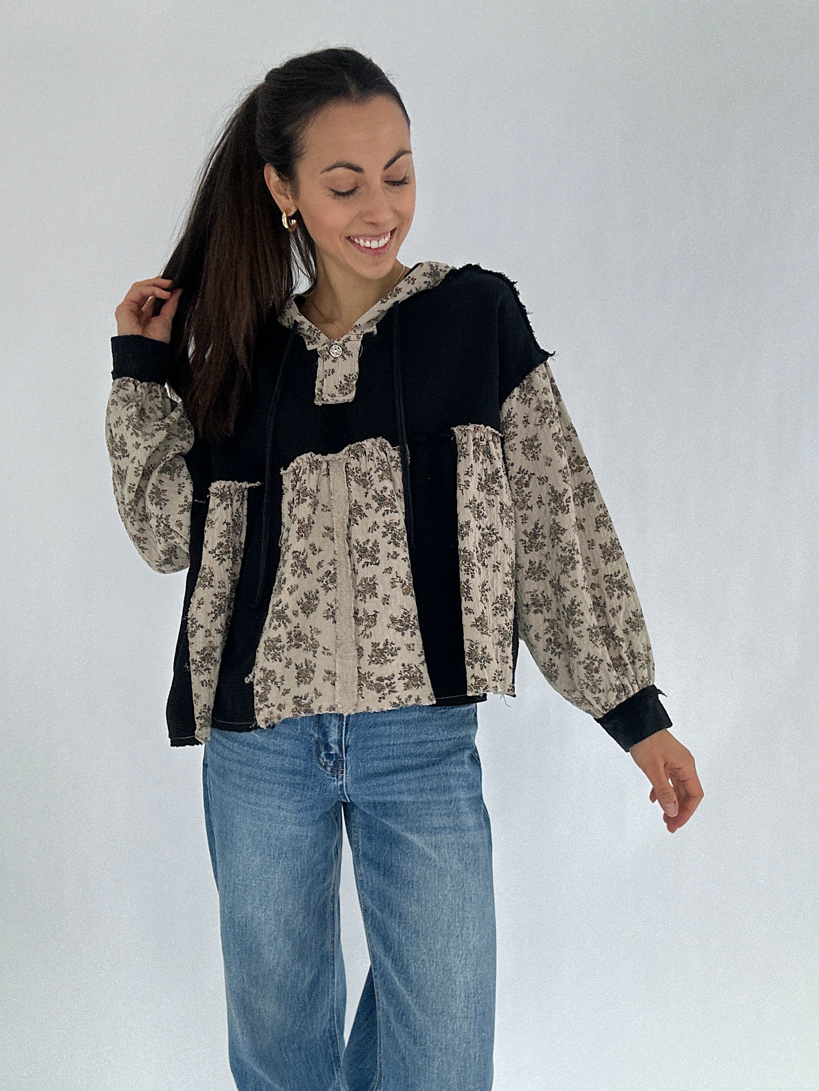 Woman wearing a black and floral-patterned hoodie top with blue jeans on a white background