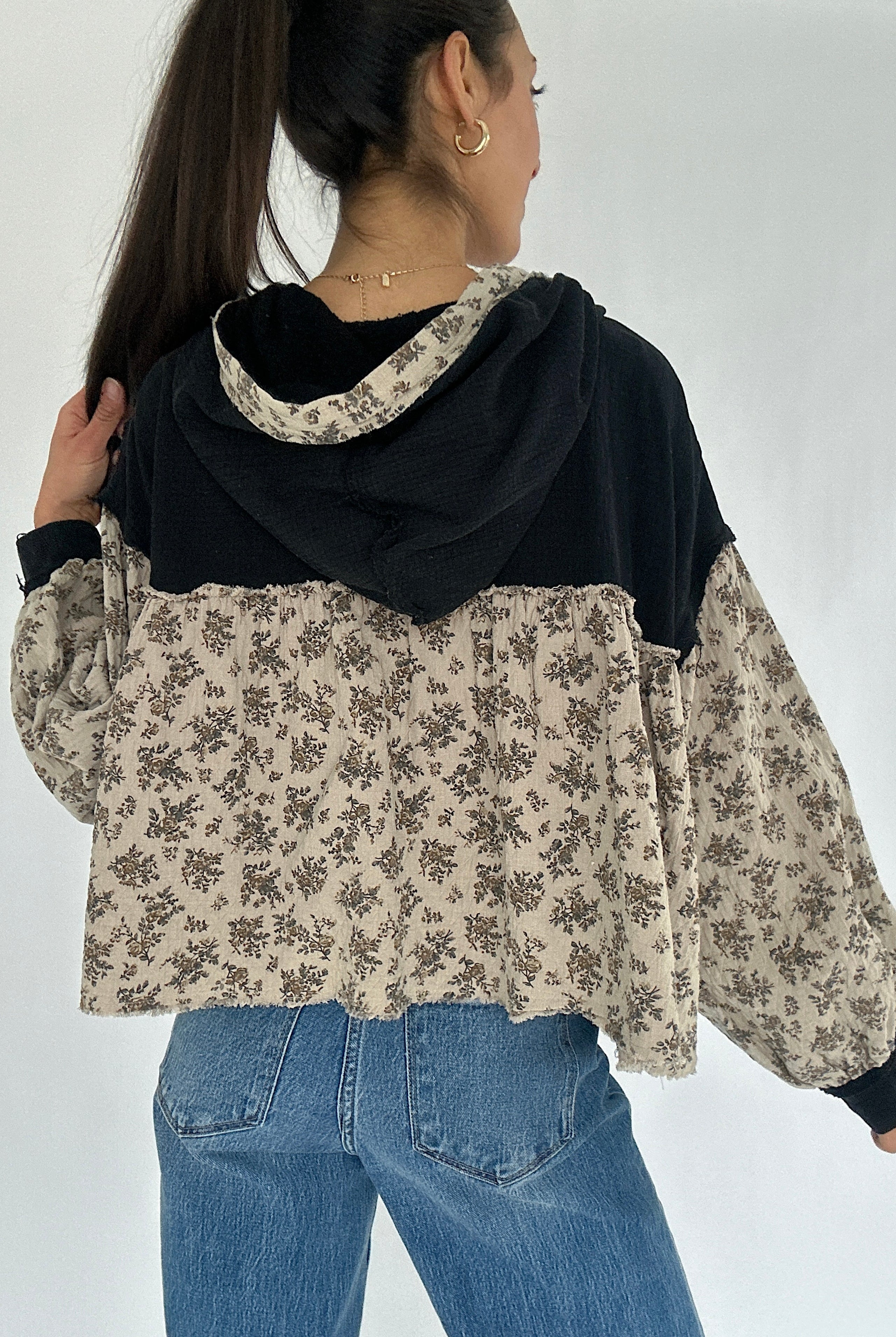Person wearing a black and beige floral-patterned hoodie top with blue jeans on a white background showing the back