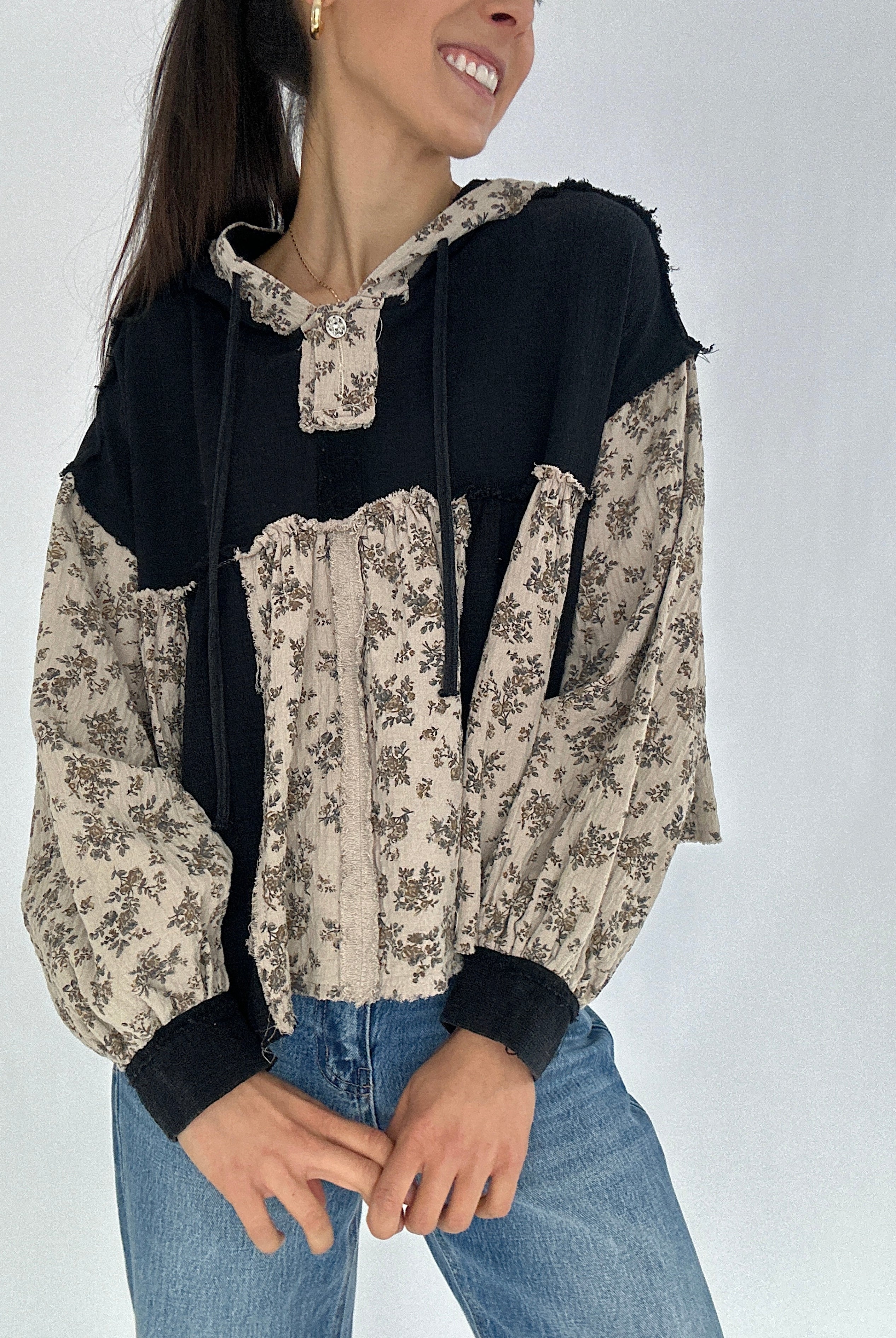 Woman wearing a black and beige floral top with blue jeans on a white background