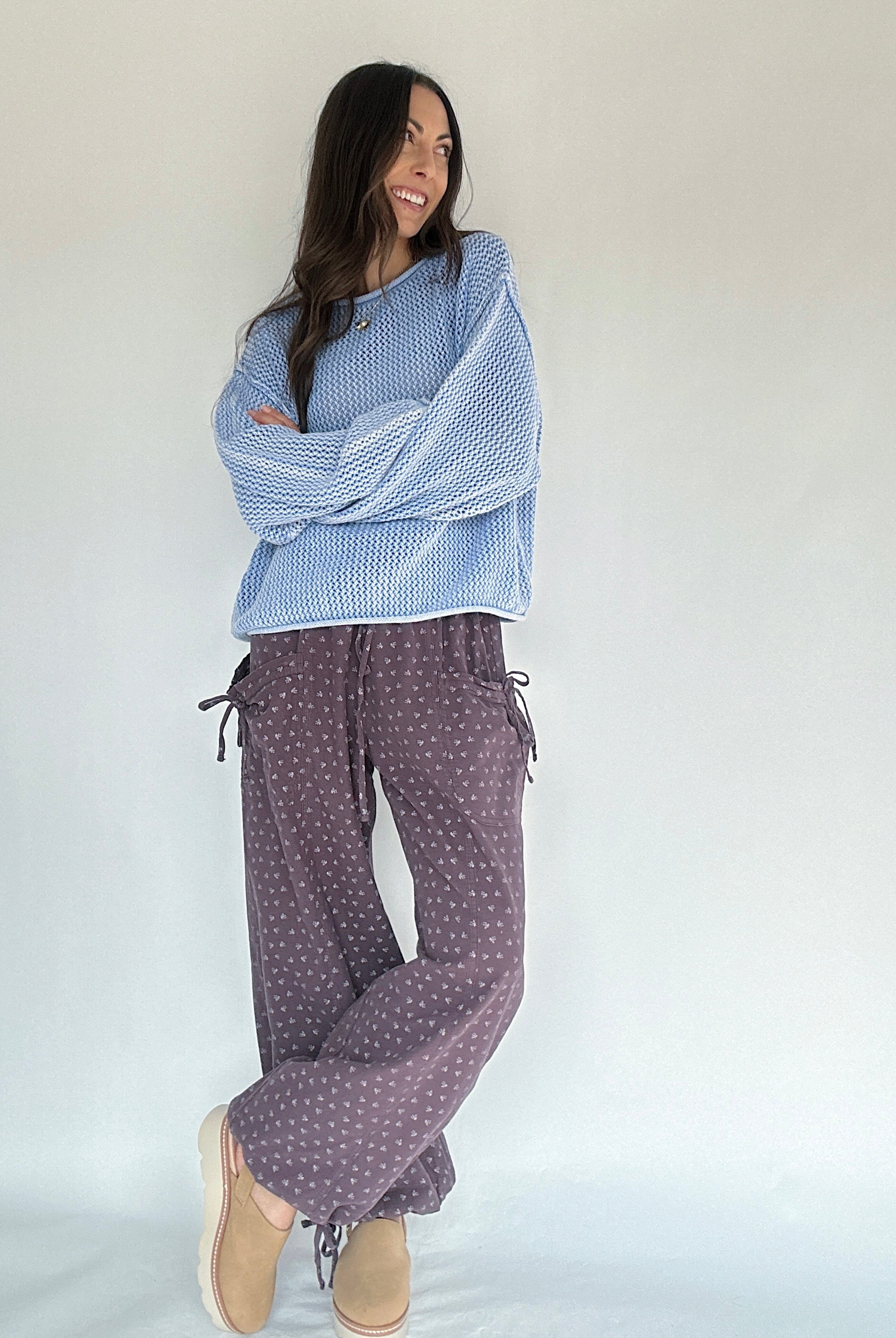 Woman wearing a blue patterned top and purple polka dot pants on a plain background