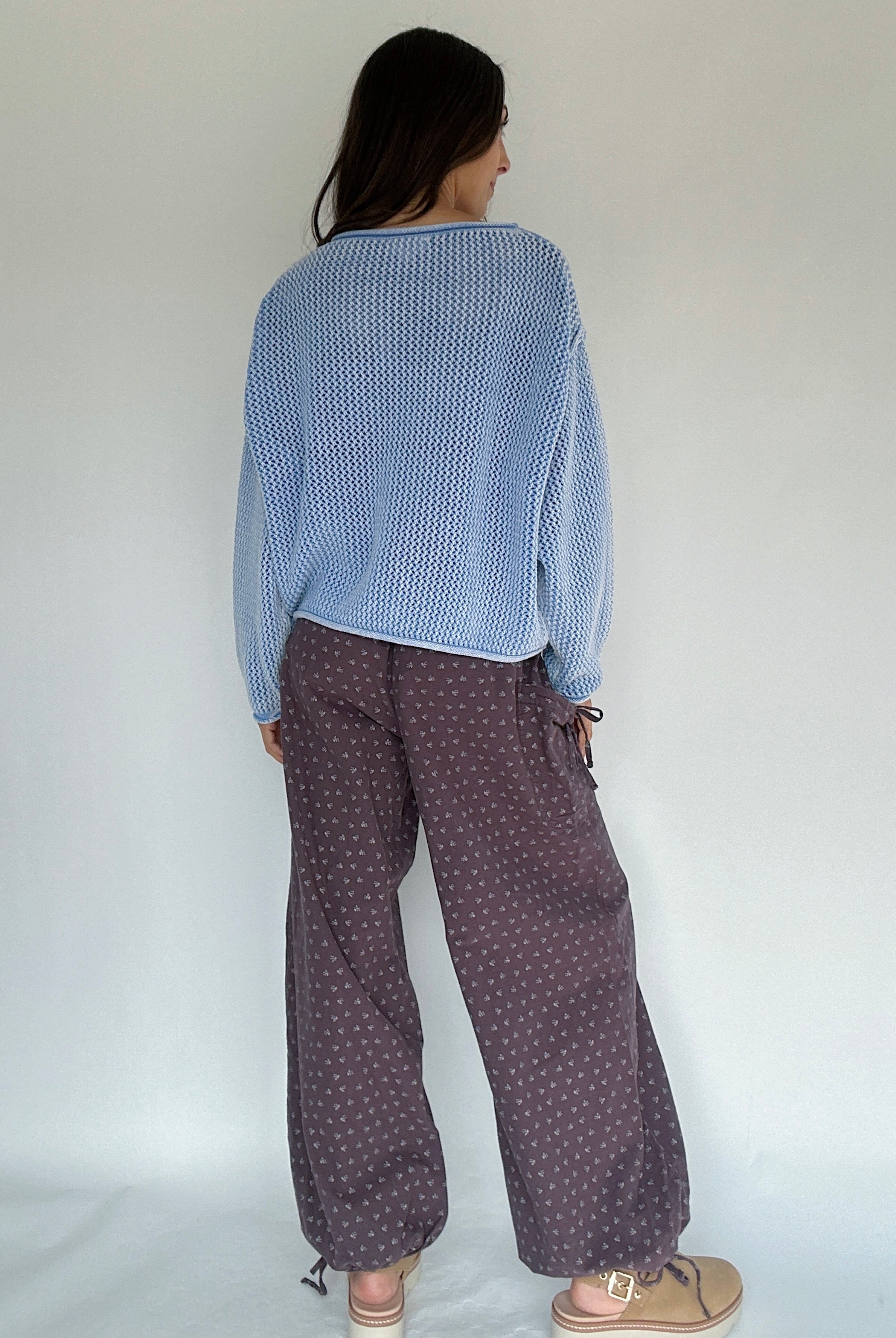Person's back wearing a blue textured sweater and patterned brown pants against a white background
