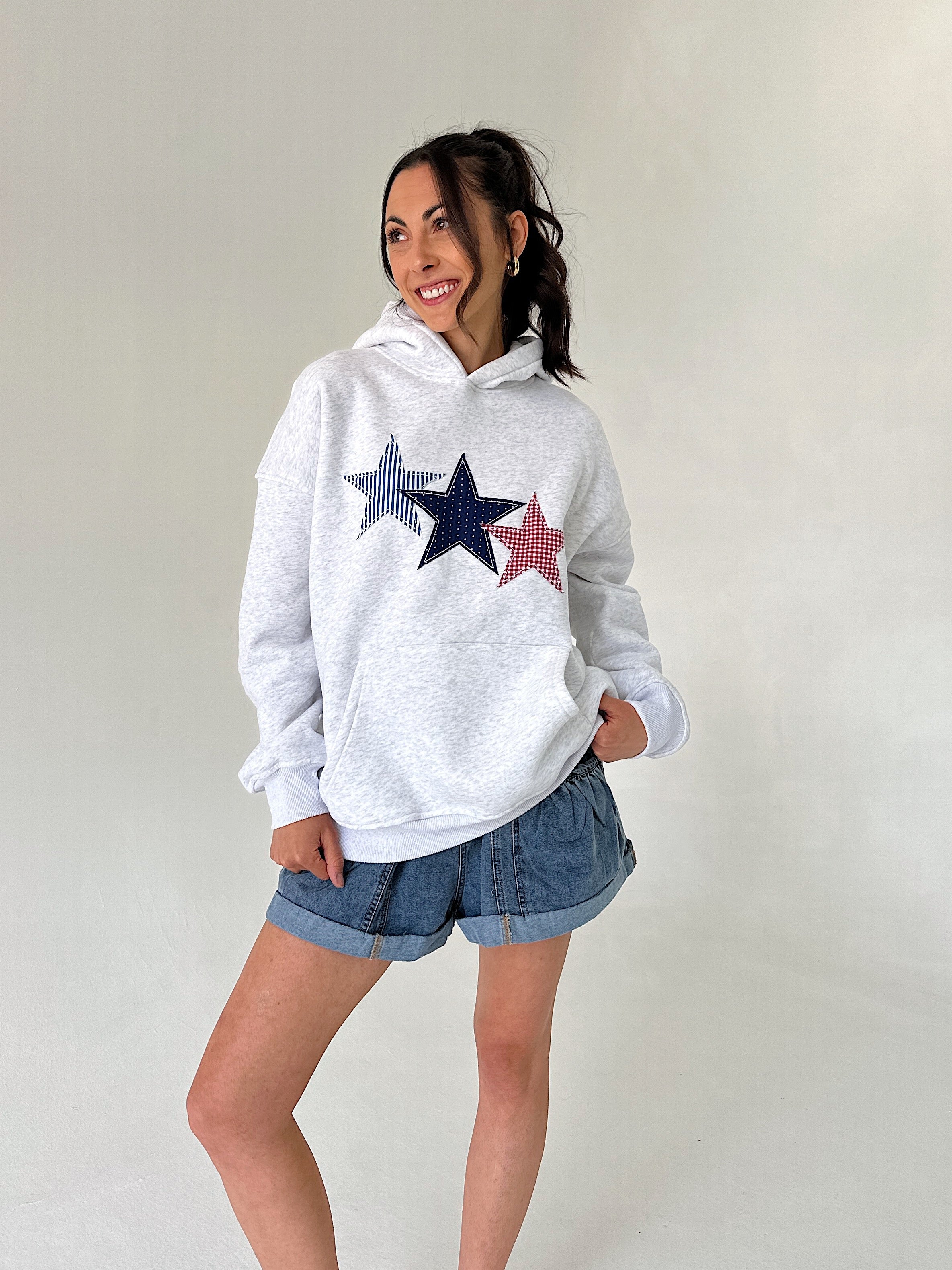 Woman wearing a white hoodie with star designs and denim shorts on a plain background