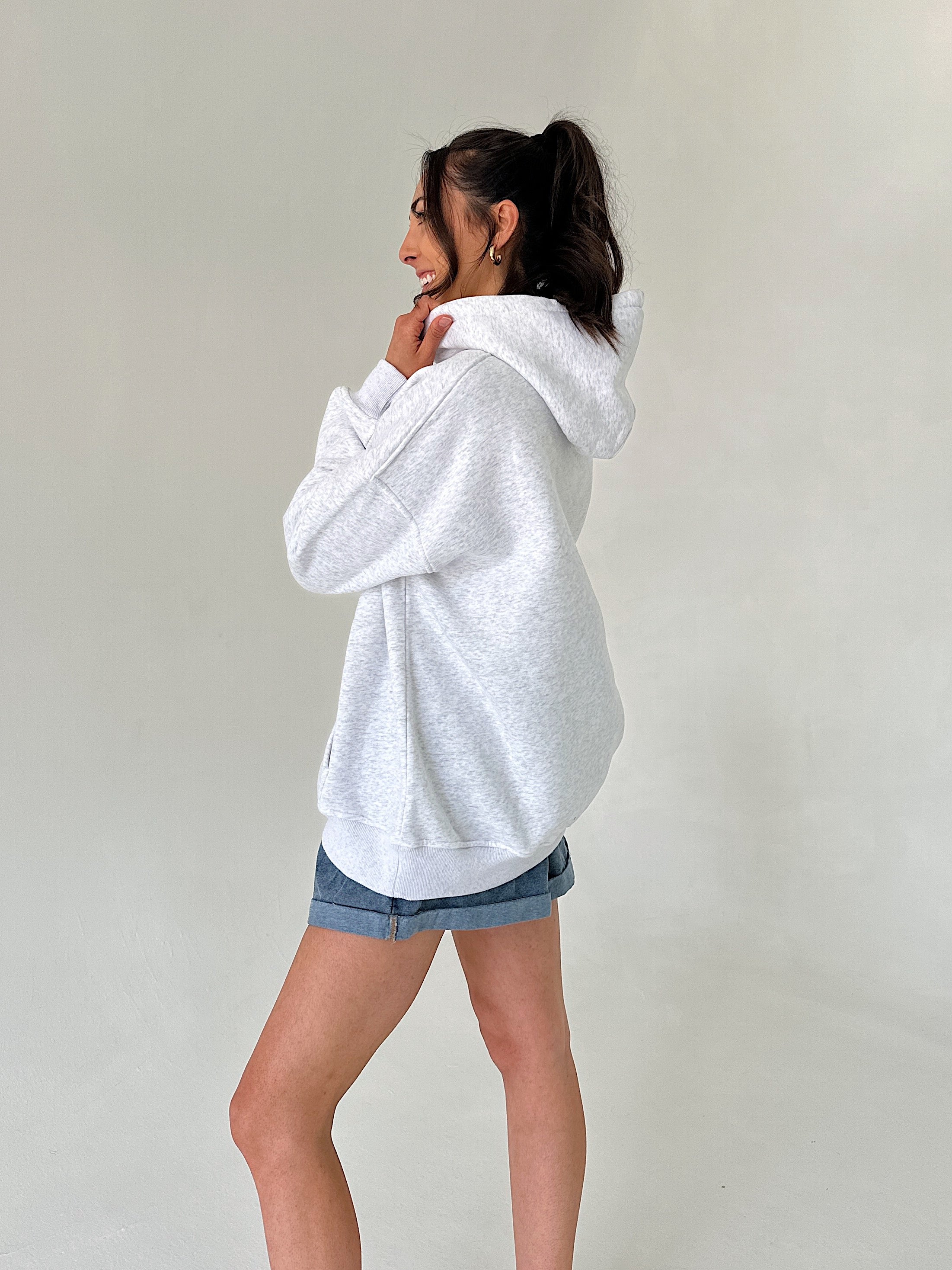 Person wearing a light gray hoodie and denim shorts against a plain background from side