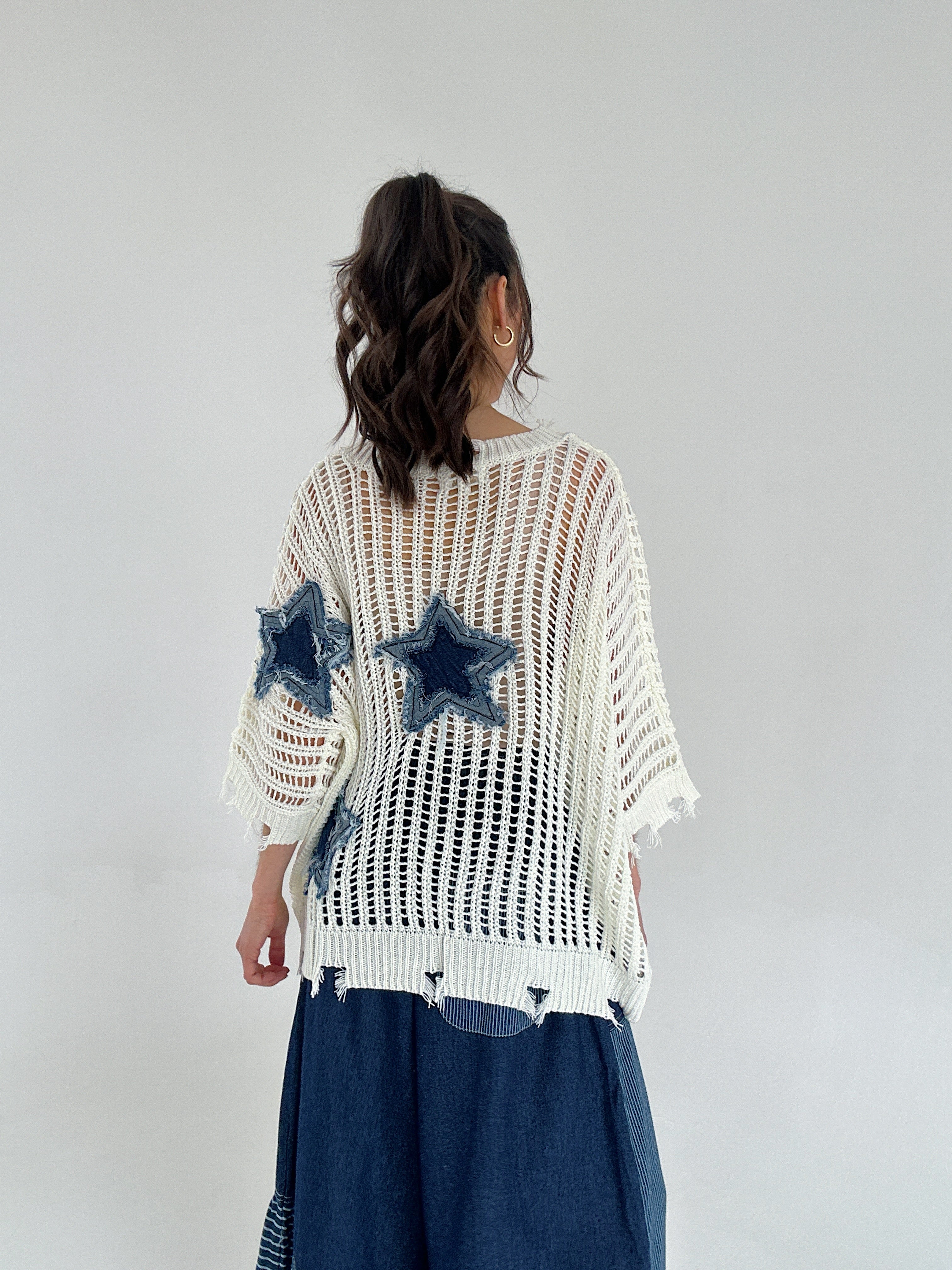 Person wearing a white knit sweater with star patterns on a plain background from back