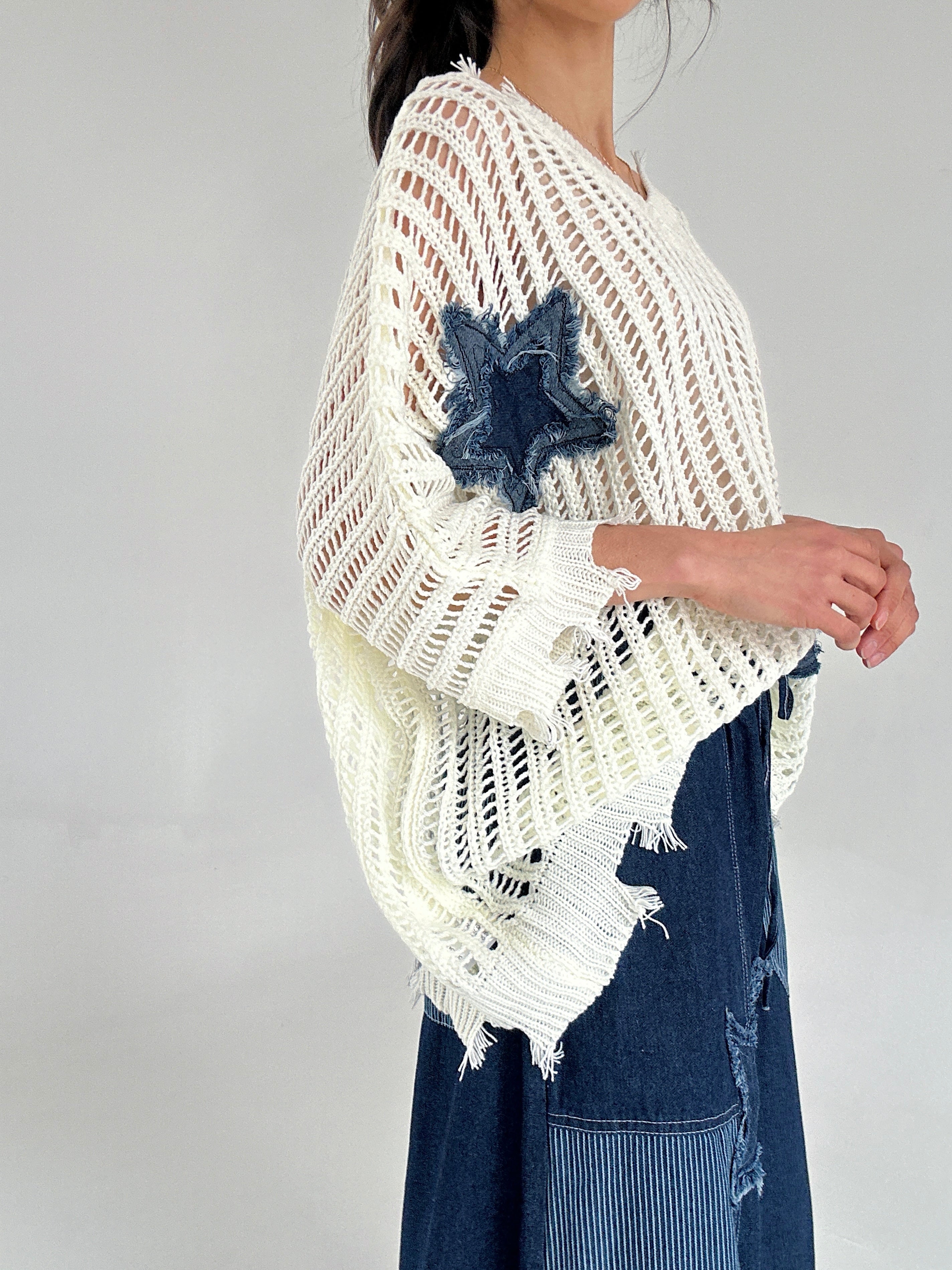 Person wearing a white knit top with denim accents on a plain background