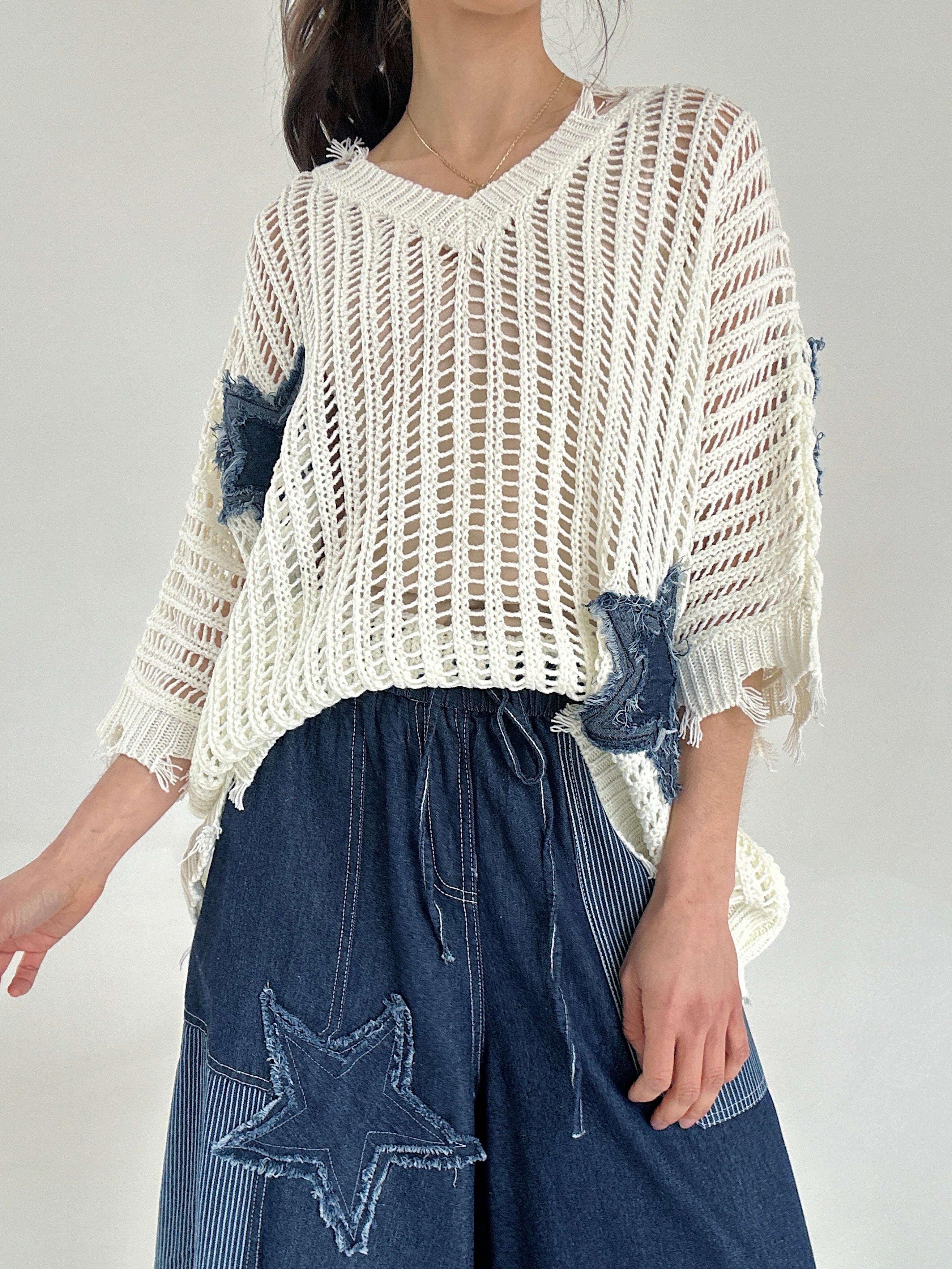 Person wearing a white knit top with star patterns on a gray background tucked