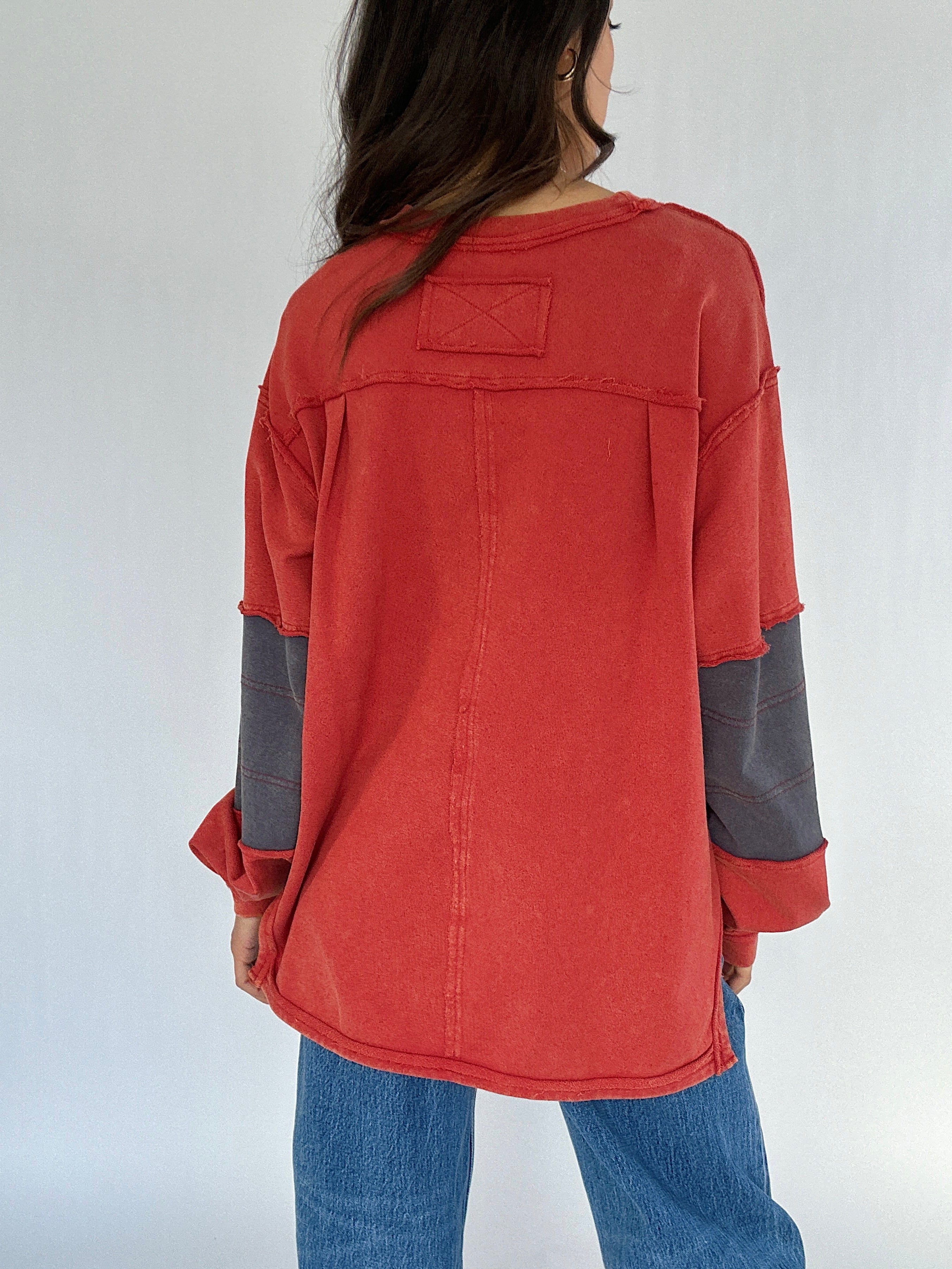 Person wearing a red and gray long-sleeve shirt with a plain background showing back seaming details