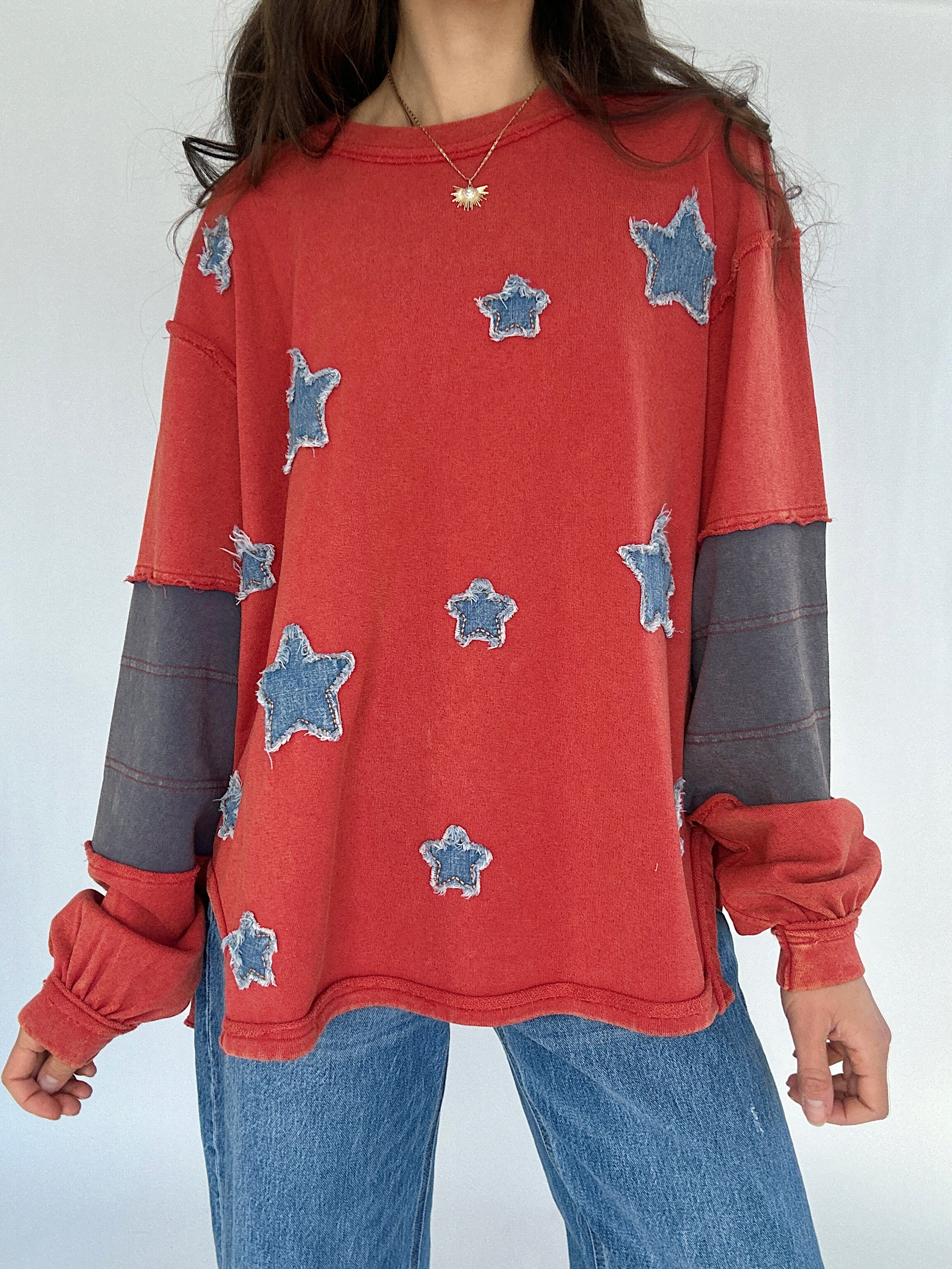Person wearing a red sweatshirt with star patterns and blue jeans on a white background