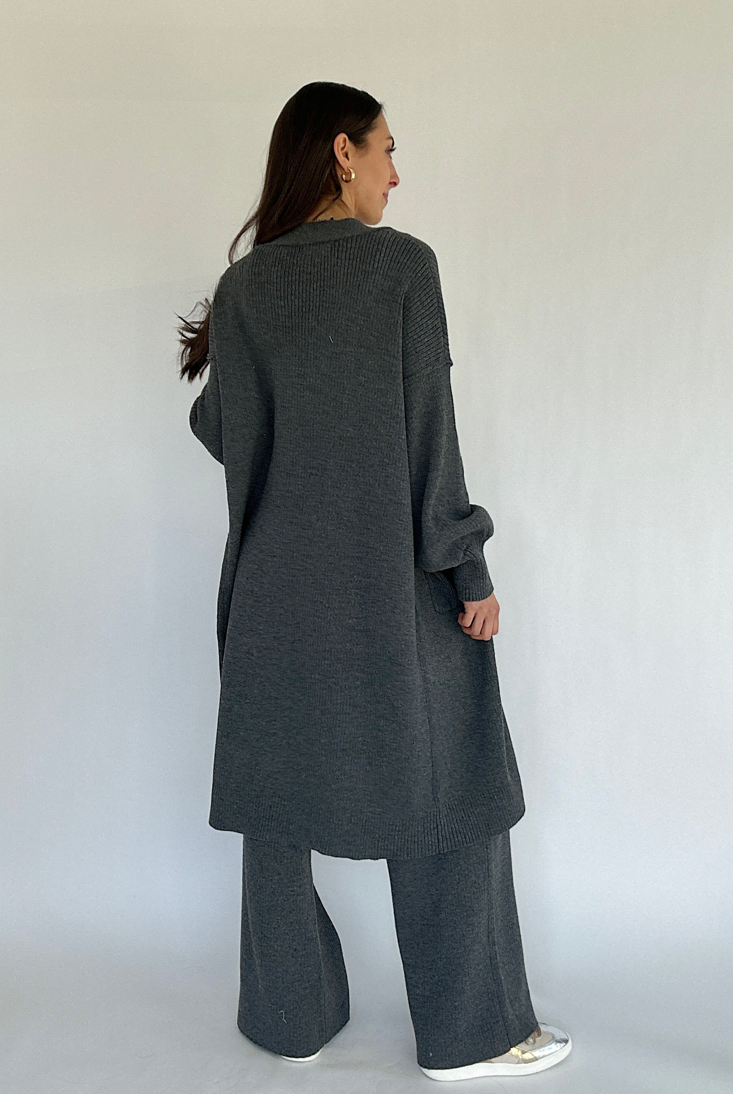Person wearing a long dark gray cardigan and pants against a white background