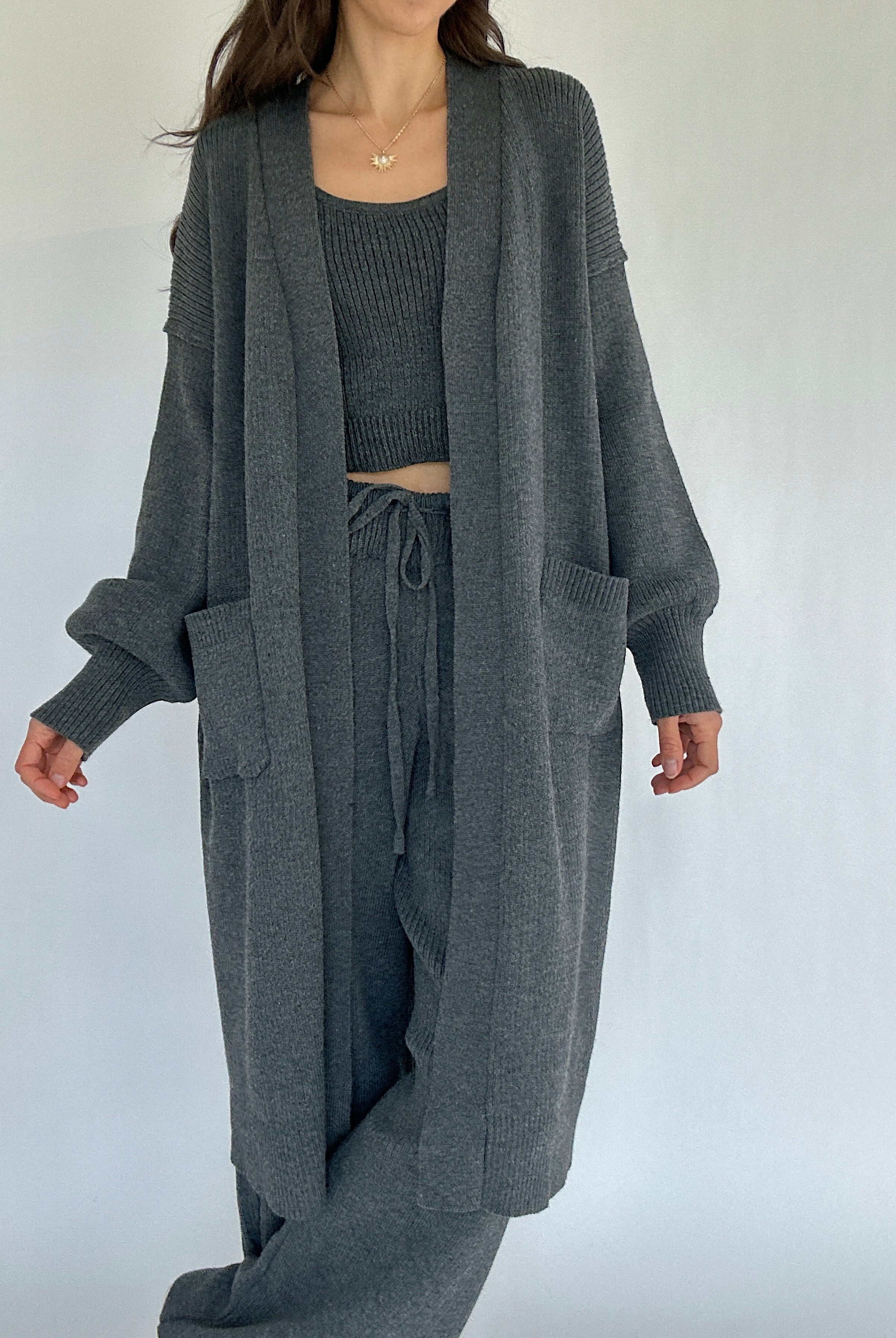 Person wearing a gray knit cardigan, top, and pants on a white background