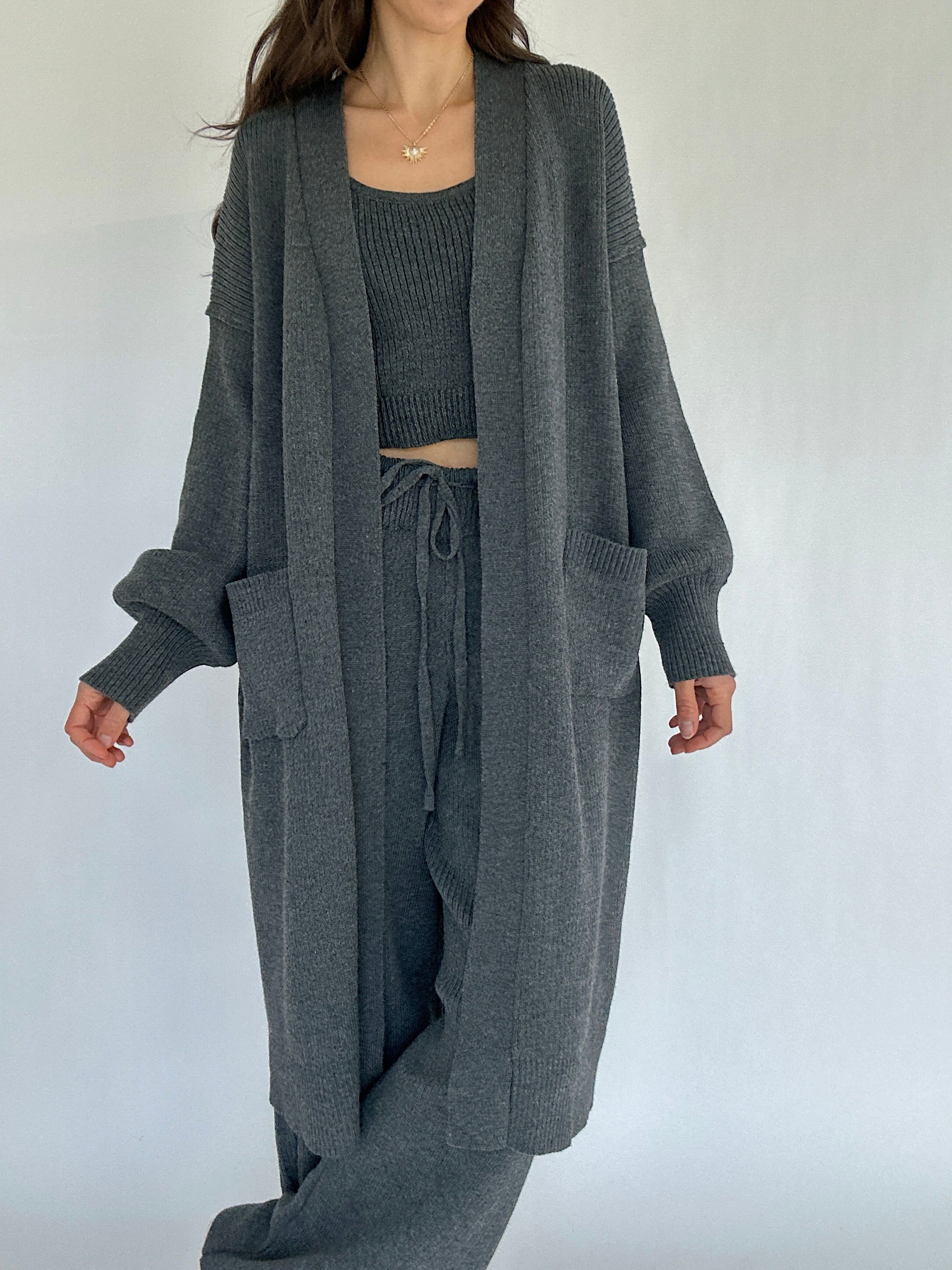 Person wearing a gray knit cardigan, top, and pants on a white background