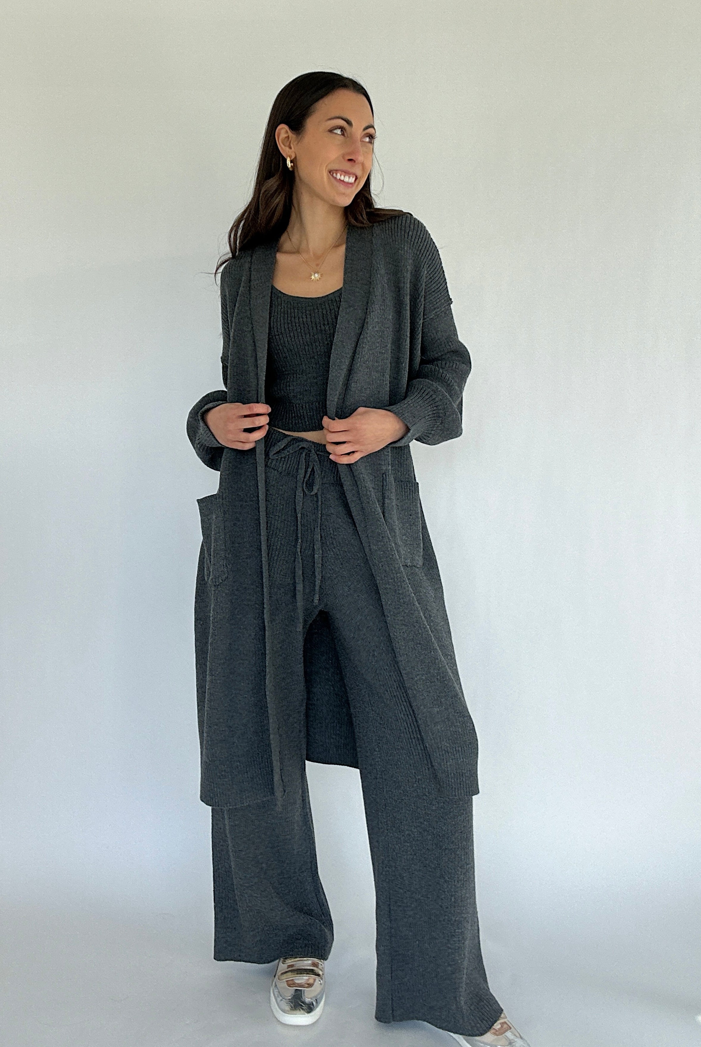 Woman wearing a gray outfit with a matching cardigan and pants against a white background