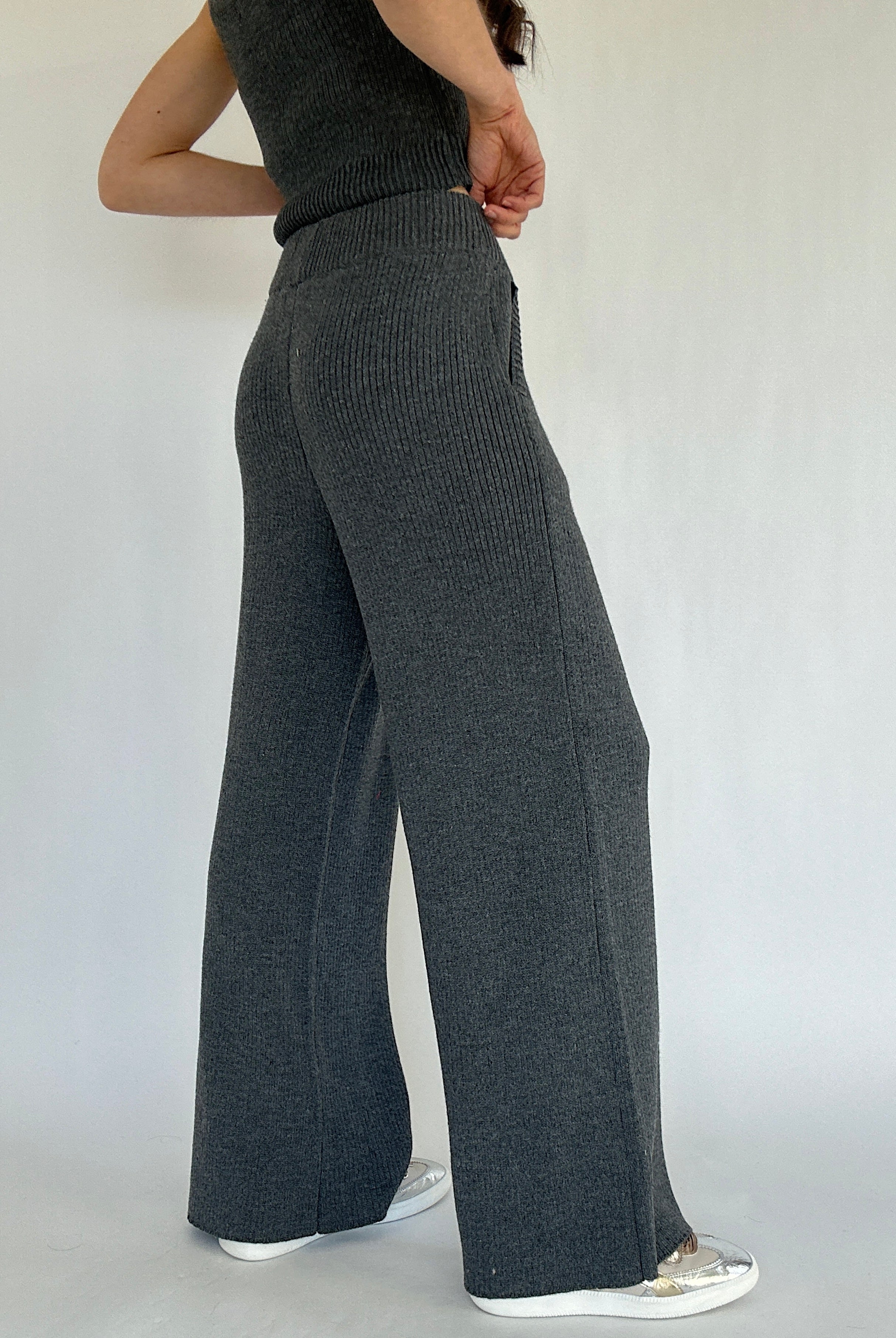 Person wearing dark gray ribbed knit pants on a plain background showing the back