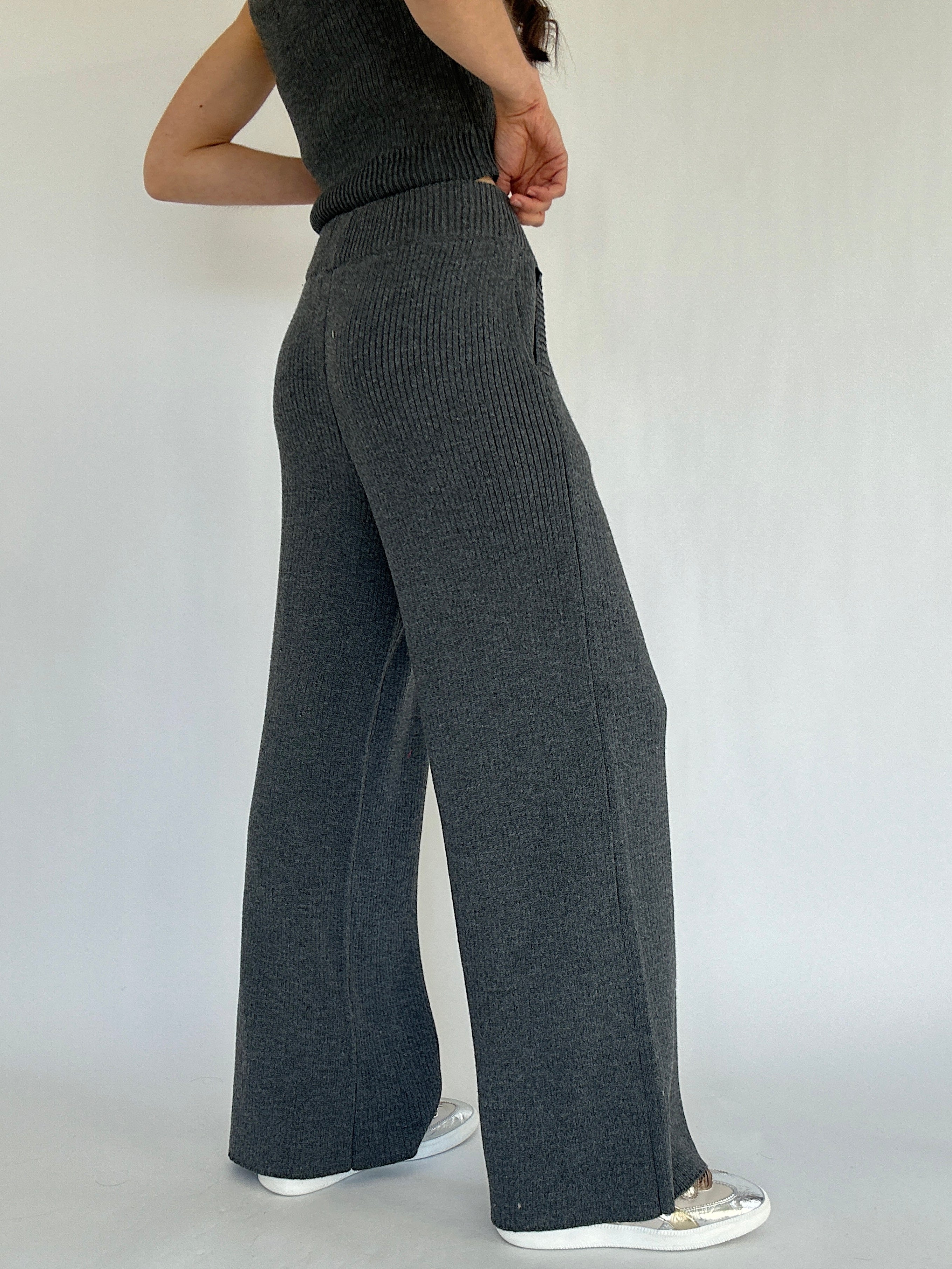 Person wearing dark gray ribbed knit pants on a plain background showing the back