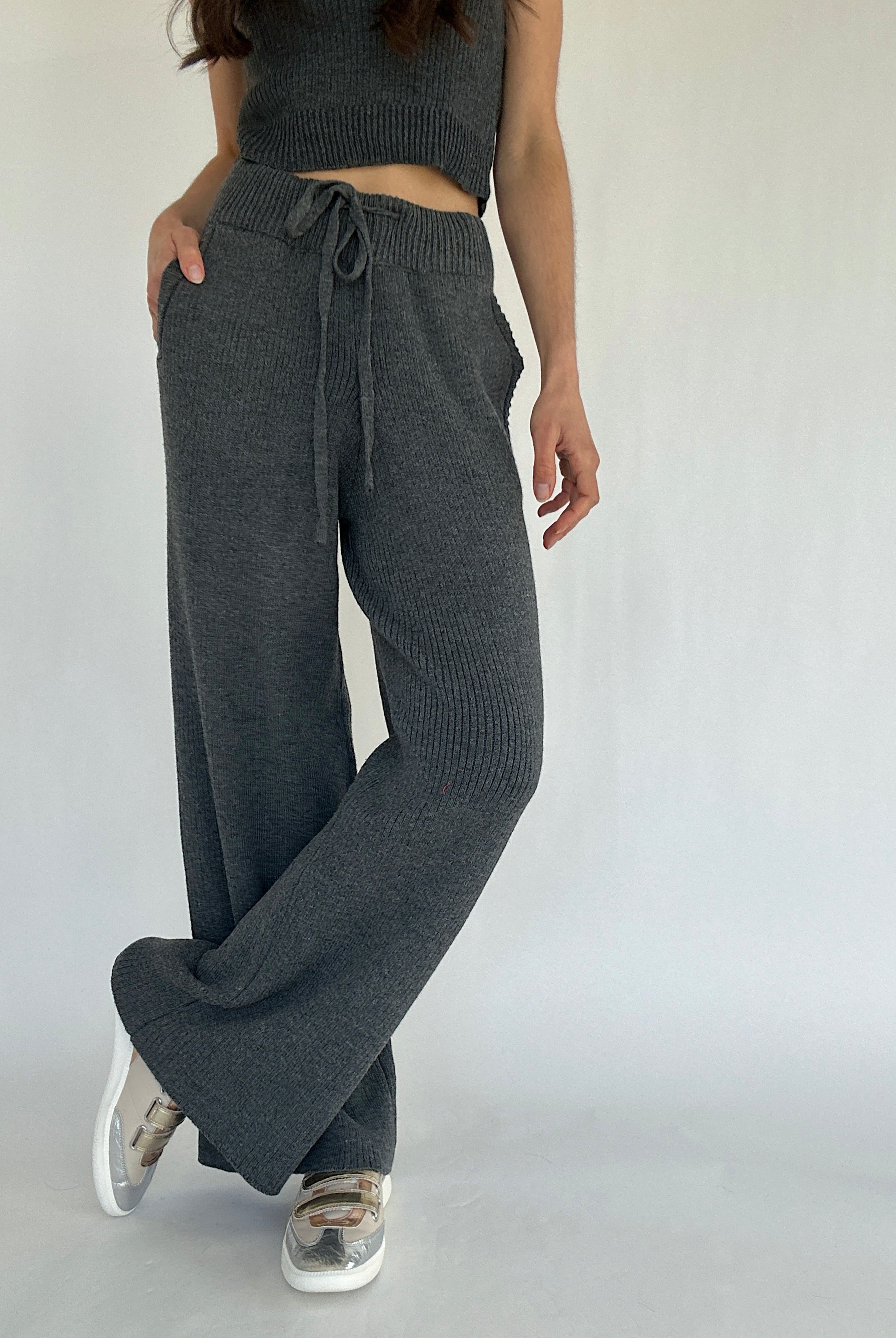 Person wearing dark gray ribbed knit pants with a tied waistband on a plain background