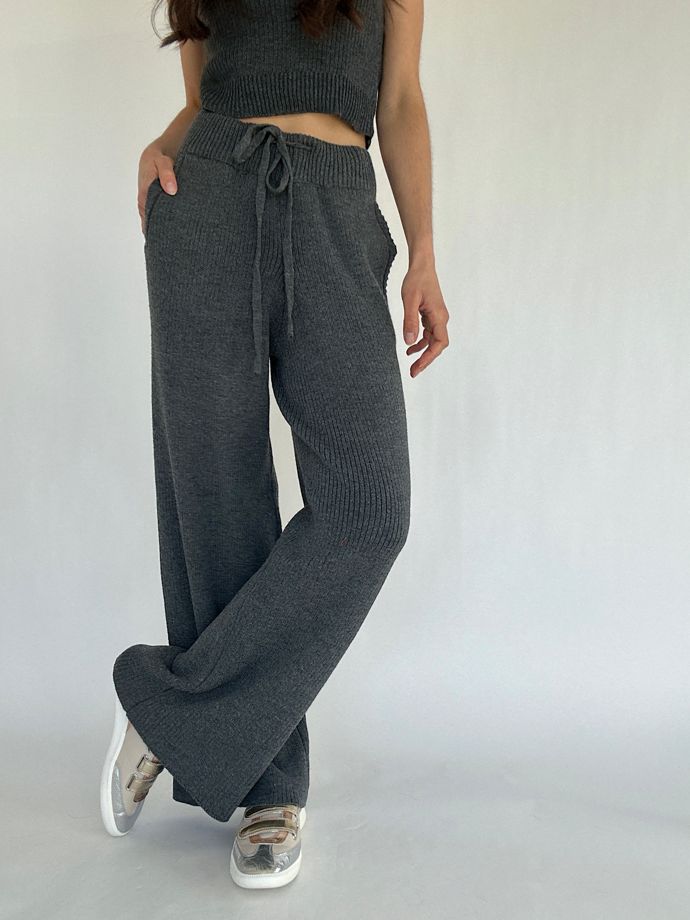 Person wearing dark gray ribbed knit pants with a tied waistband on a plain background