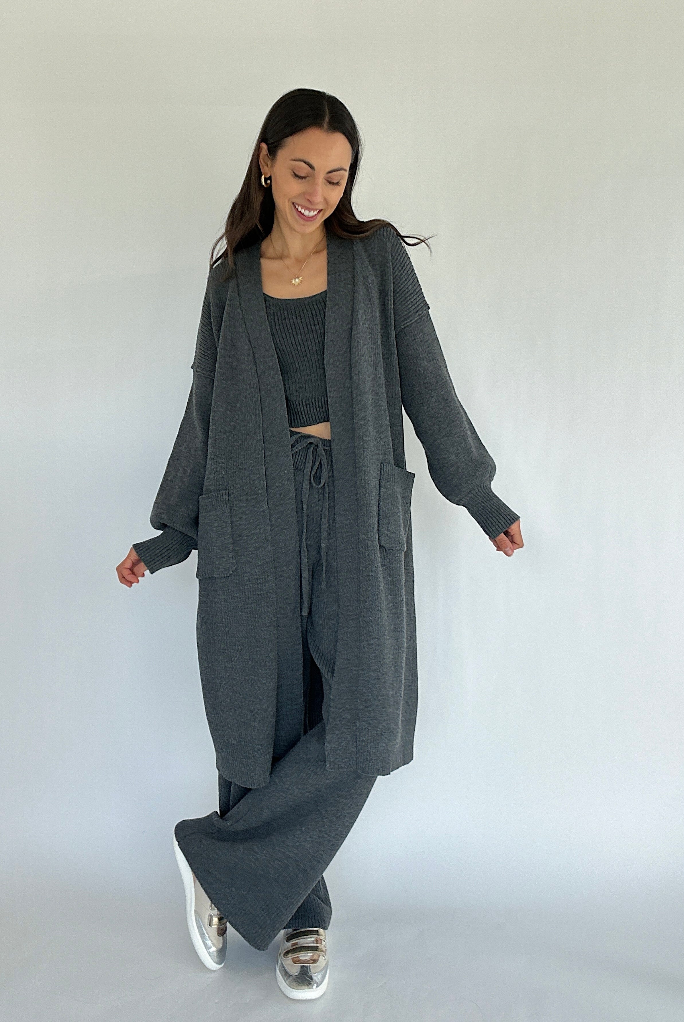 Woman wearing a matching gray long cardigan, top, and pants on a white background