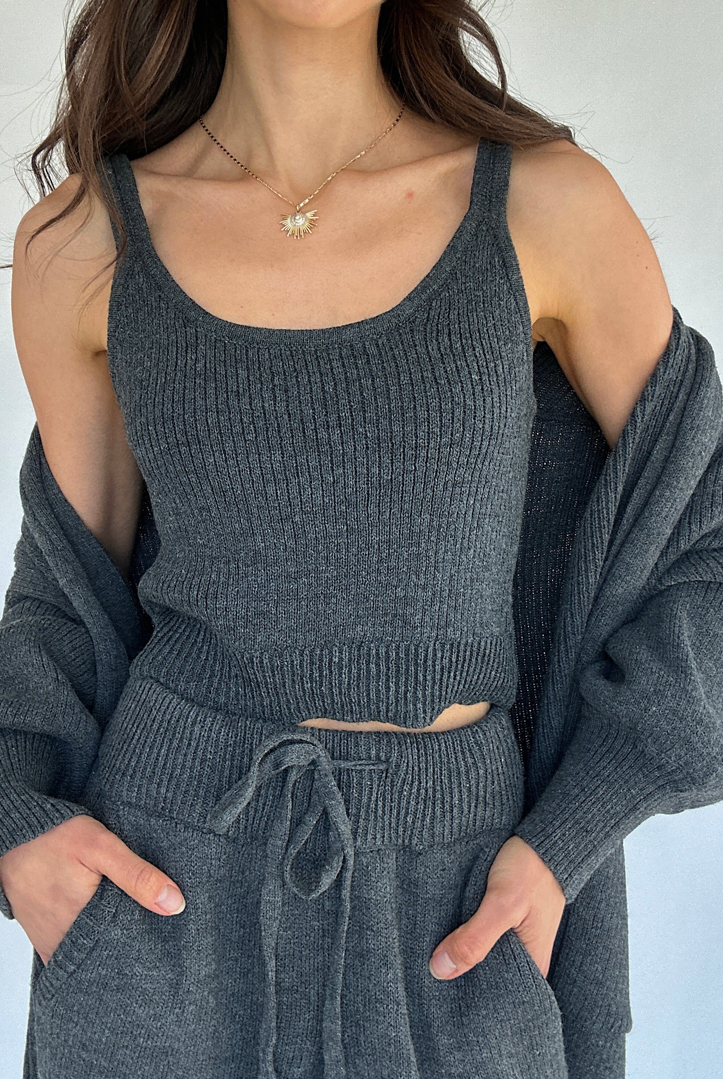 Person wearing a gray knit tank top with a matching cardigan against a white background