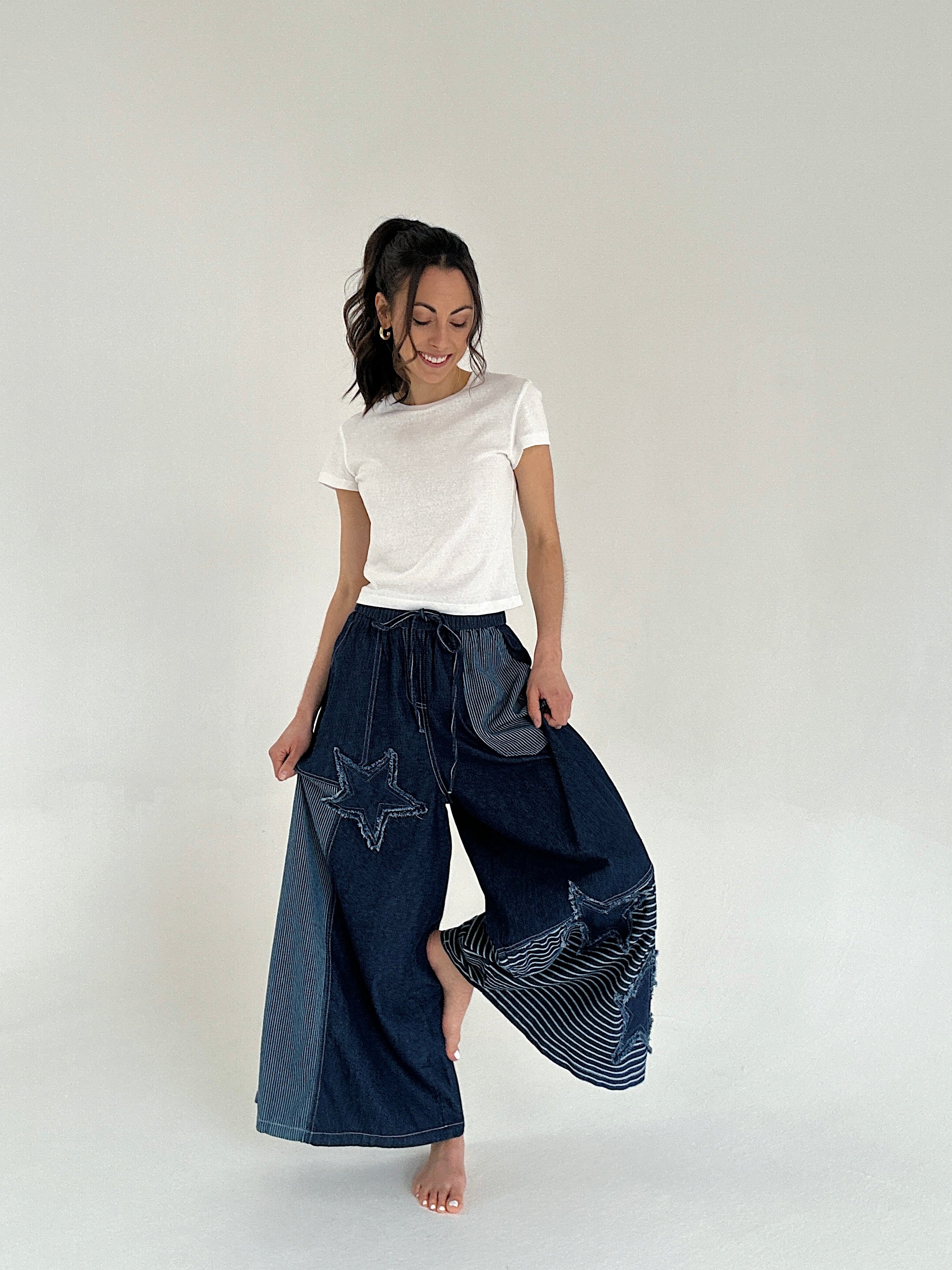 Woman wearing a white t-shirt and dark blue wide-leg pants with star patterns on a plain background