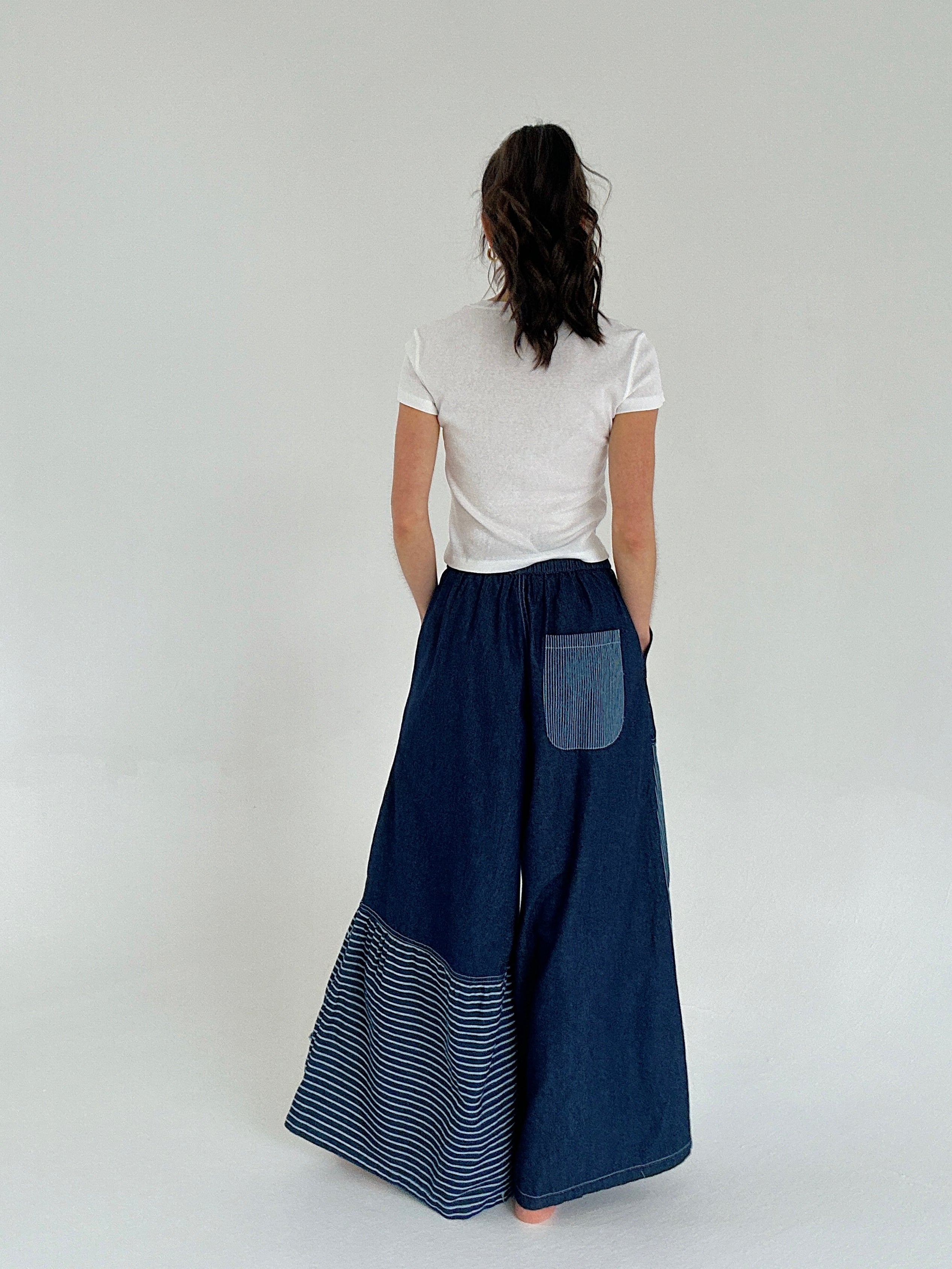 Person wearing a white top and blue denim skirt with a pocket on a plain background