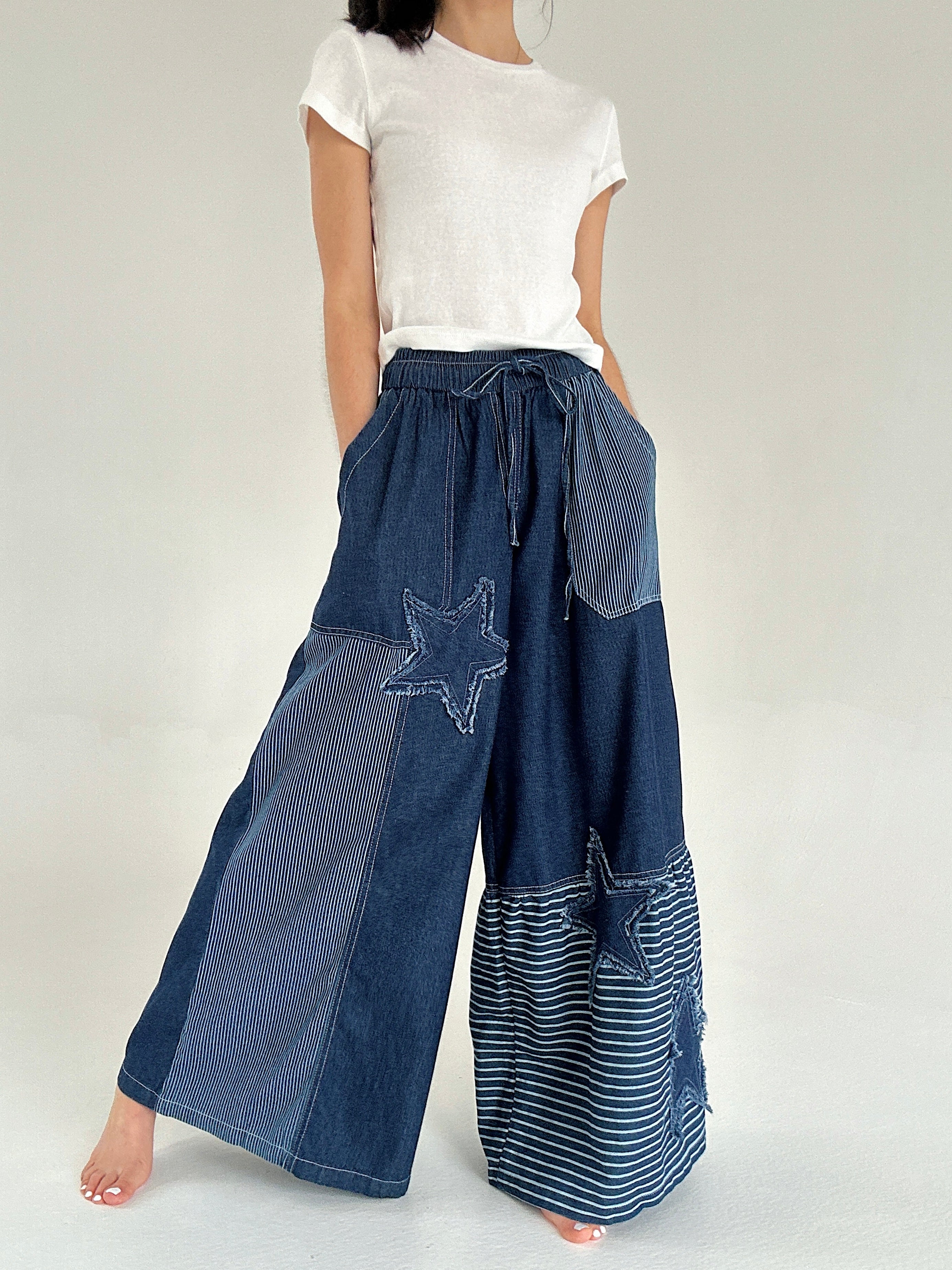 Person wearing blue patchwork pants with star designs on a white background