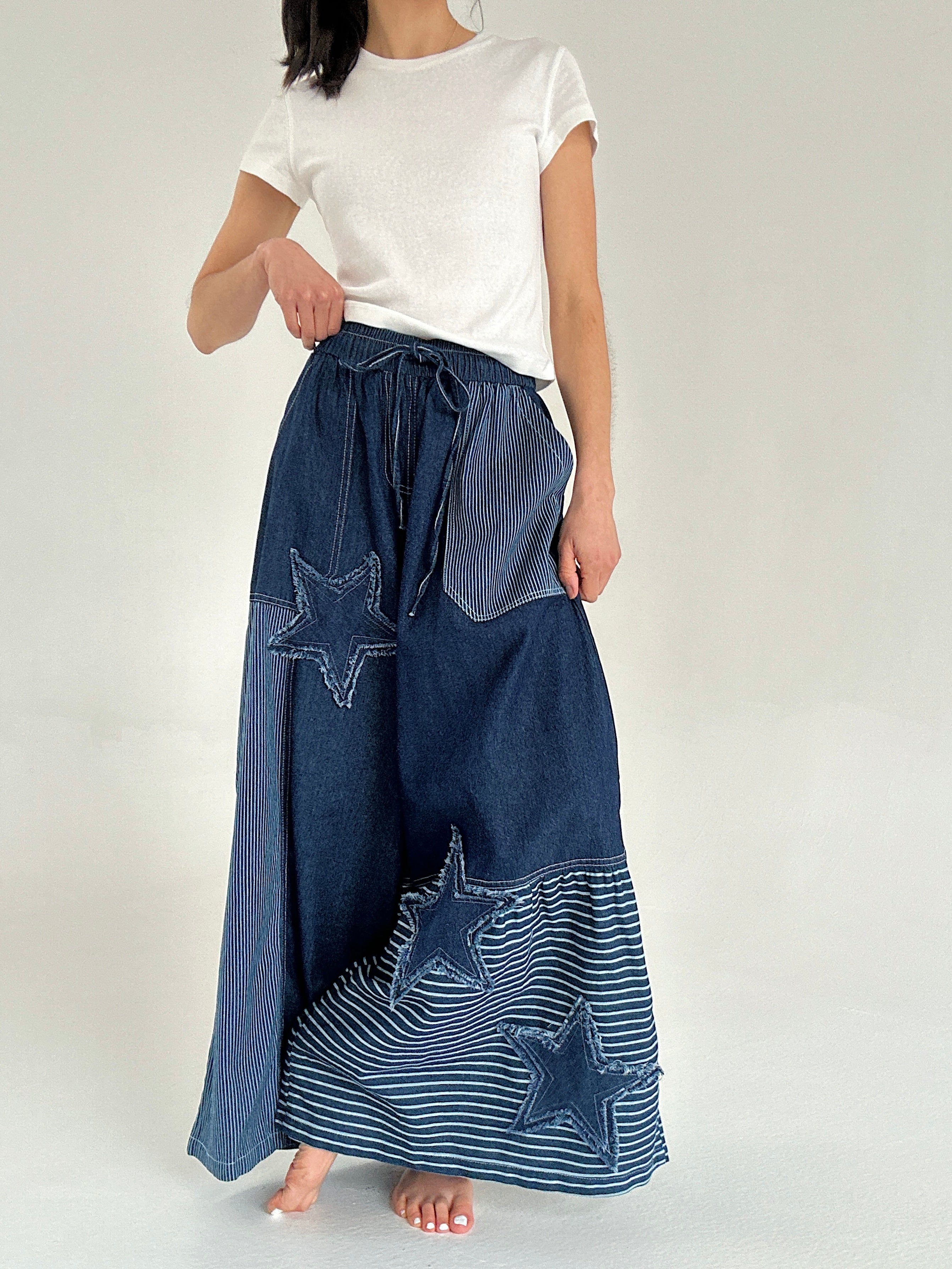 Person wearing a white t-shirt and blue denim pants with star patterns on a plain background