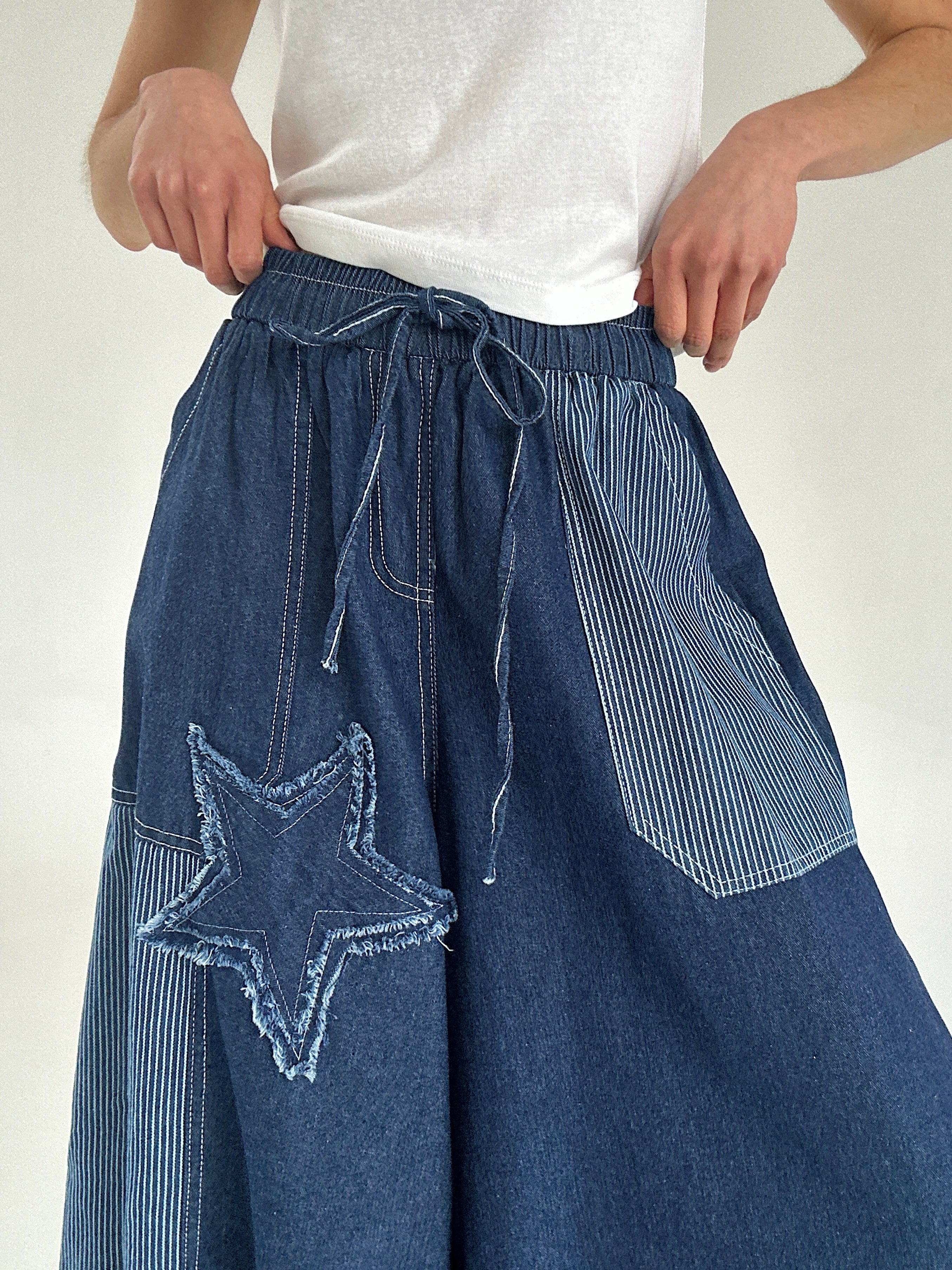 Blue denim pants with a star patch worn by a person on a white background