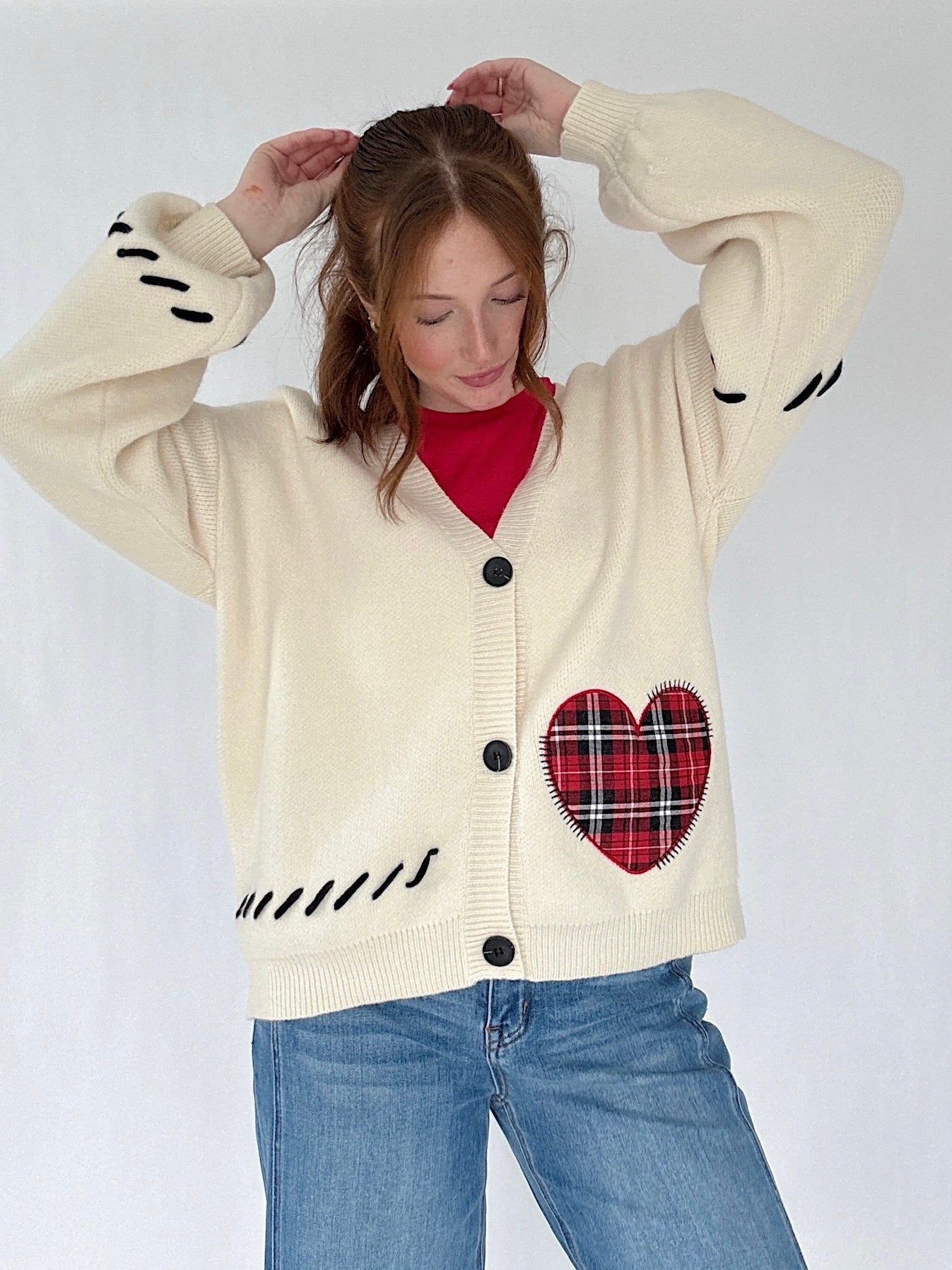 Person wearing a cream cardigan with a red plaid heart design on a white background