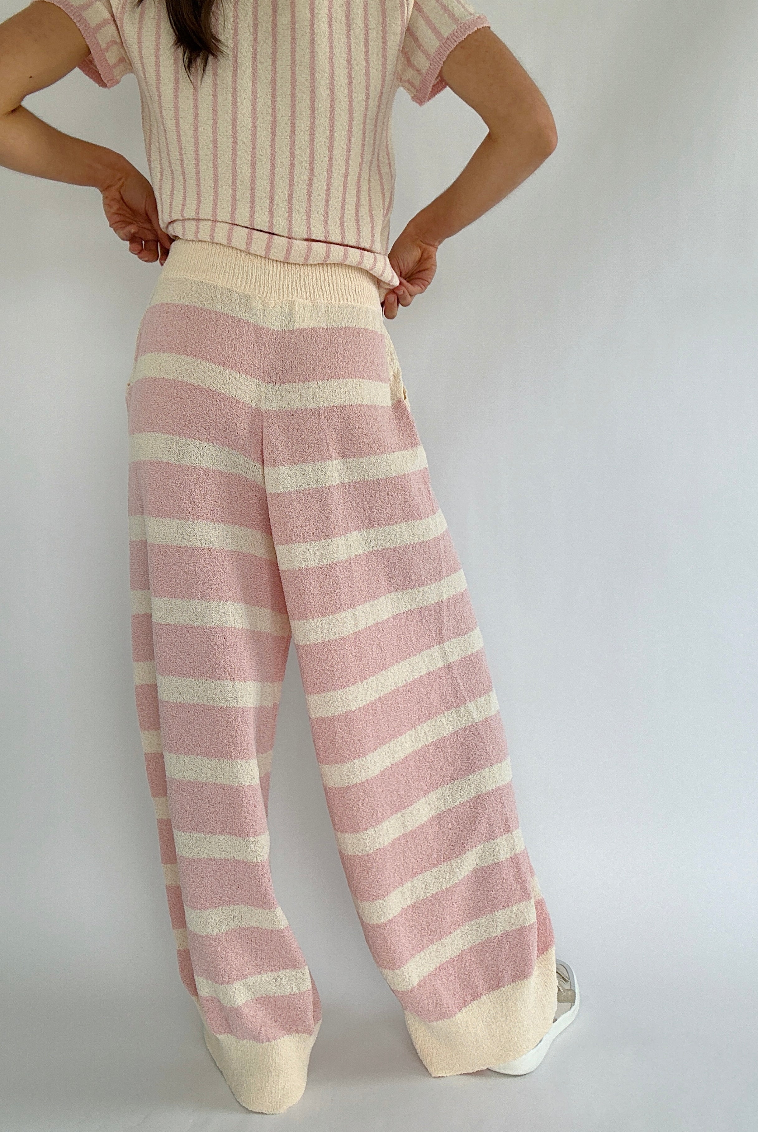 Person wearing a striped outfit with pink and cream pants on a plain background