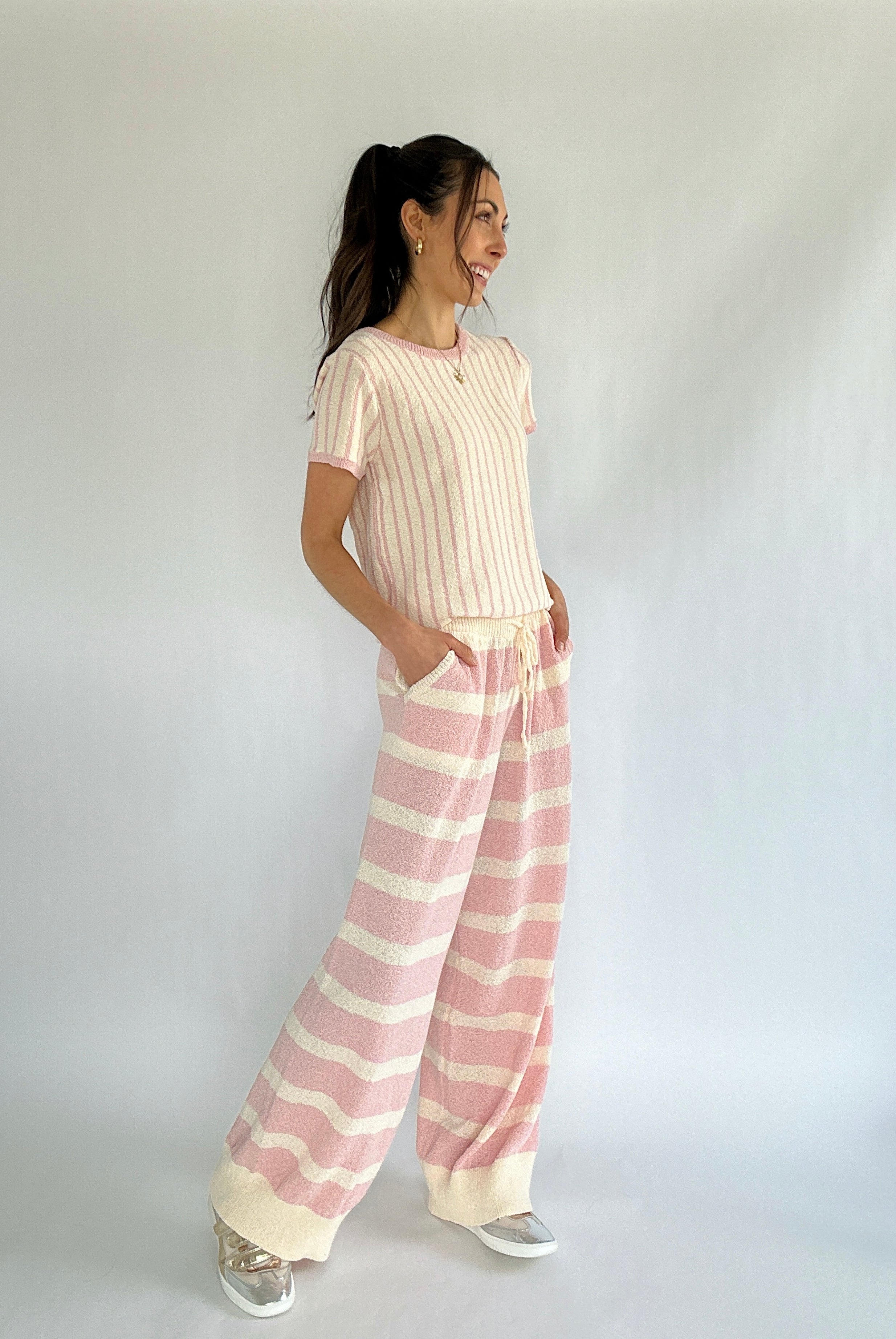 Woman wearing a cream top and pink striped pants against a white background