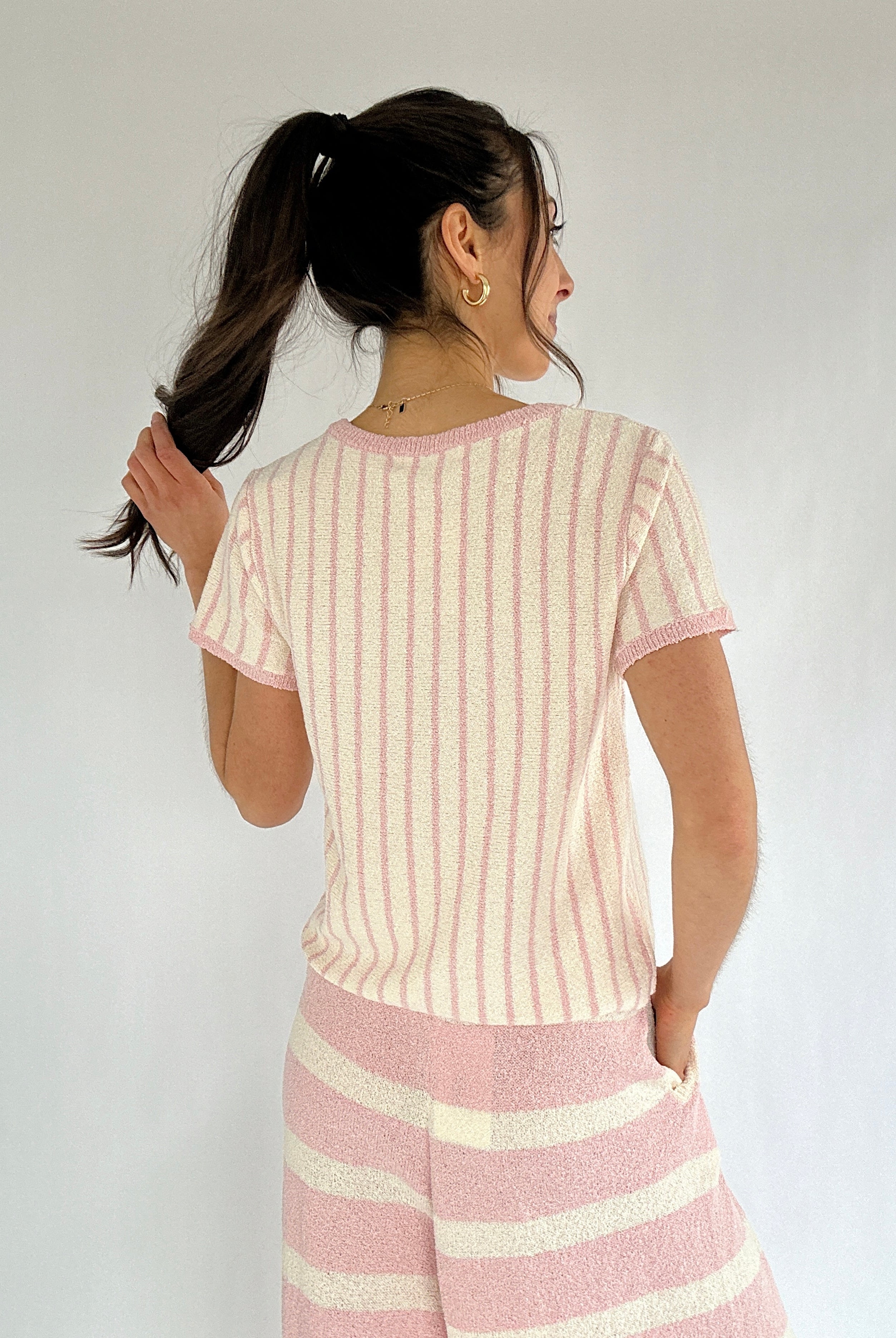 Woman wearing a pink and white striped outfit against a plain background showing back