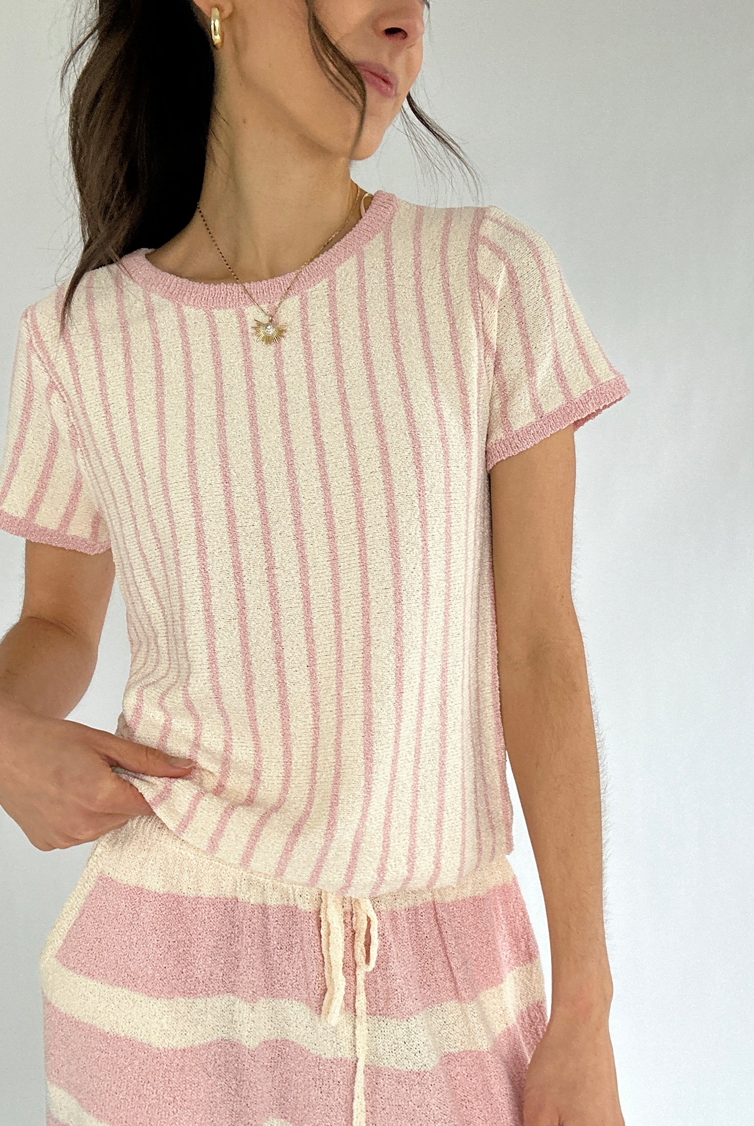 Woman wearing a pink and white striped knit short sleeve top and matching pants against a plain background